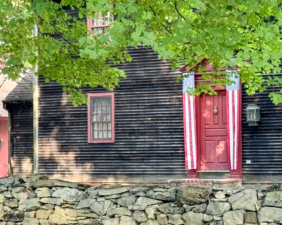 colonial-house-green-foliage-black-exterior-red-trim-stone-wall-americana