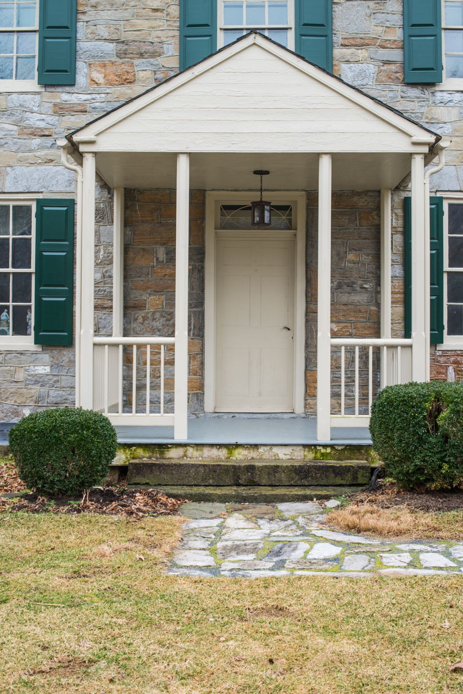 colonial-stone-house-entrance-with-white-porch-green-shutters-flagstone-path-traditional-american-architecture