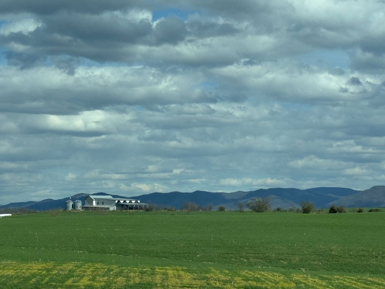 farm-buildings-green-field-mountain-backdrop-cloudy-sky