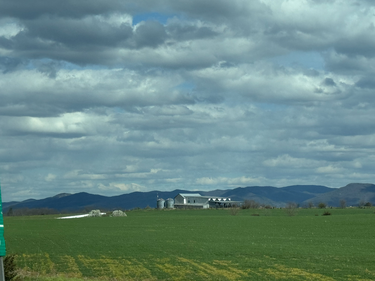 farm-buildings-green-field-mountain-backdrop-dramatic-clouds-rural-landscape-grain-silos-scenic-countryside-spring-pasture-moody-sky-agricultural-scene