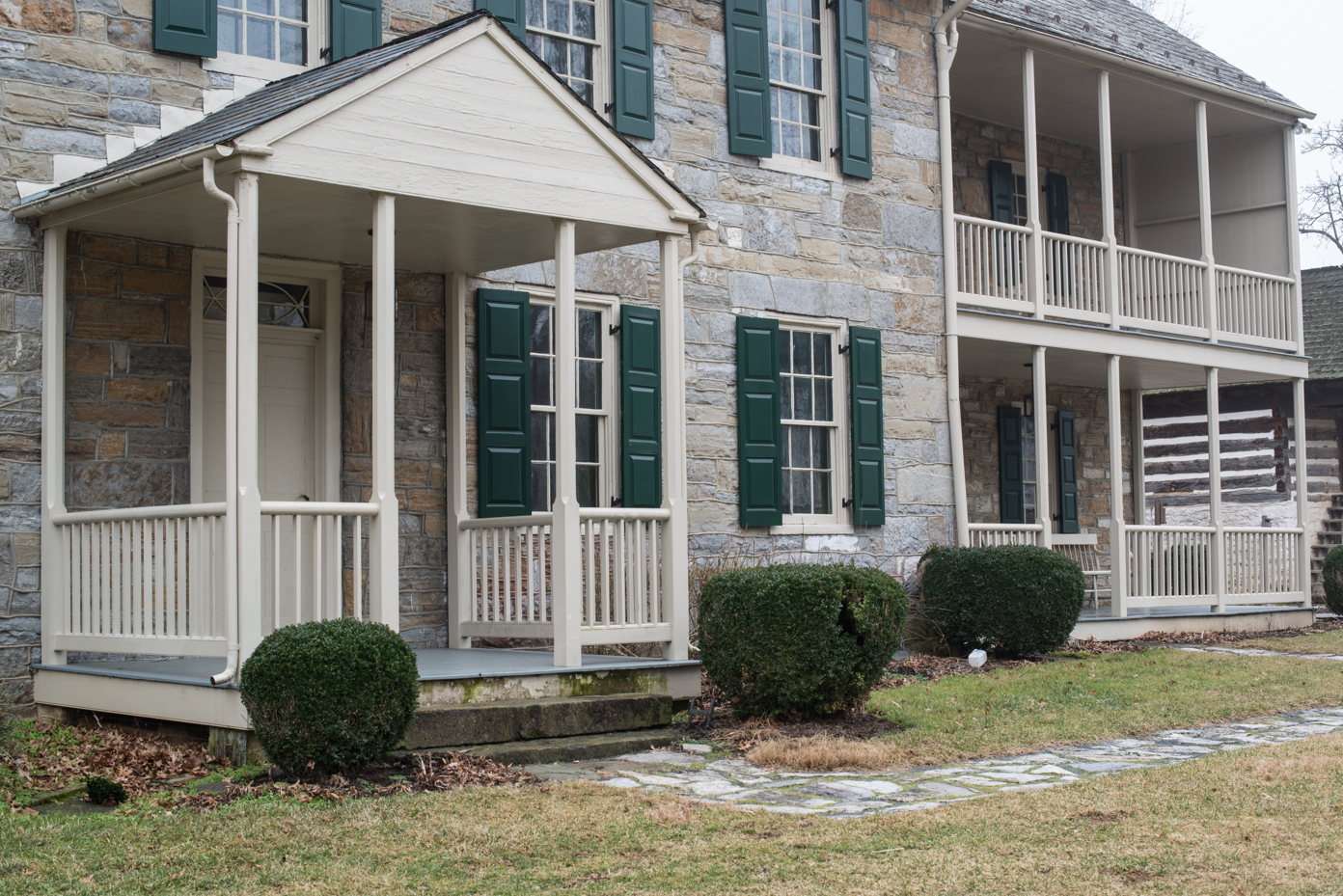 historic-stone-house-with-multiple-porches-green-shutters-colonial-american-architecture-landscaped-yard