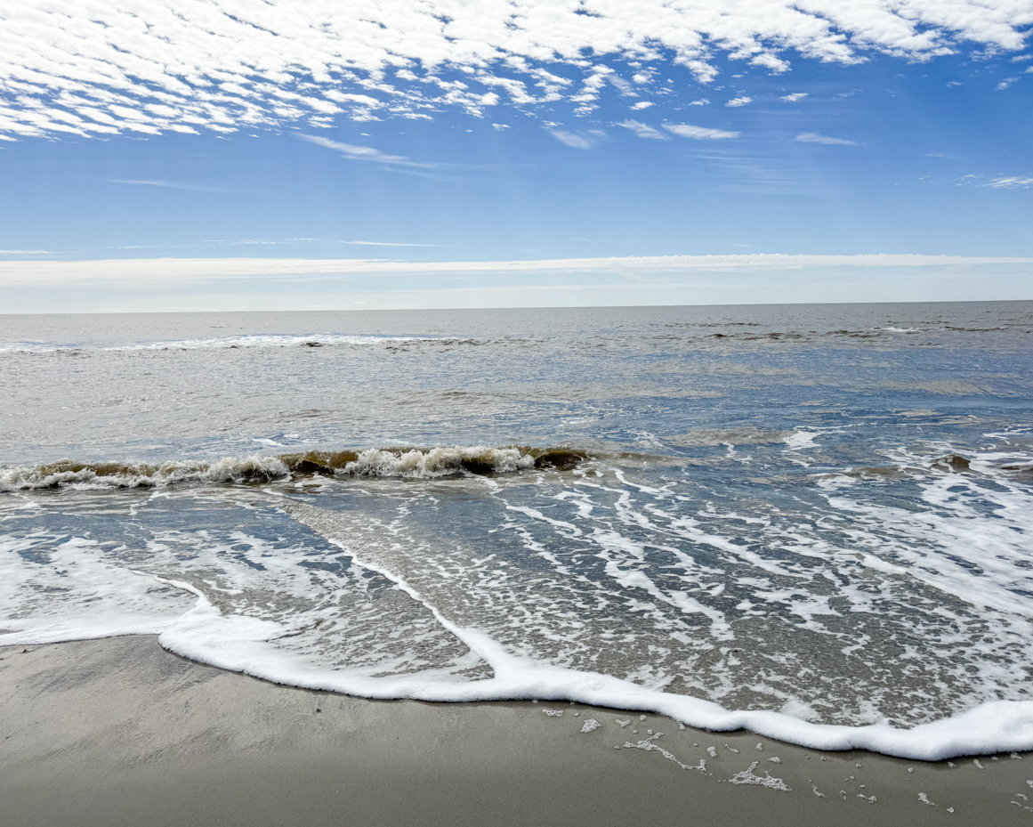 gentle-ocean-waves-washing-onto-sandy-beach-under-a-bright-blue-sky-with-scattered-clouds