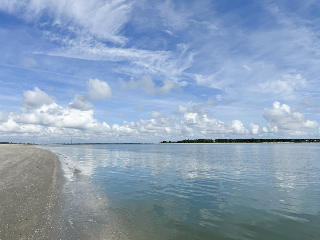 serene-beach-with-calm-water-sandy-shoreline-and-blue-sky-filled-with-white-clouds