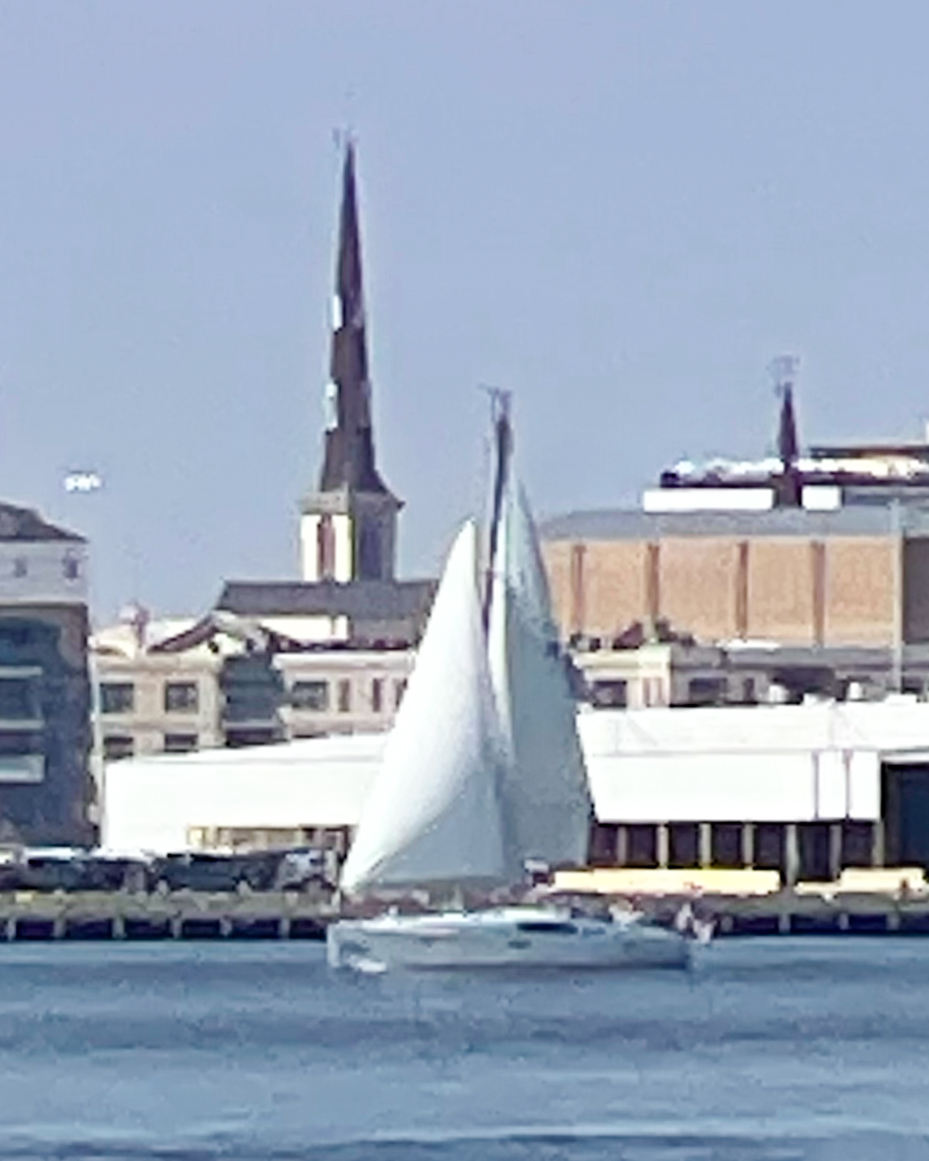 sailboat-on-a-calm-waterway-with-distant-buildings-and-a-church-steeple-under-a-clear-sky