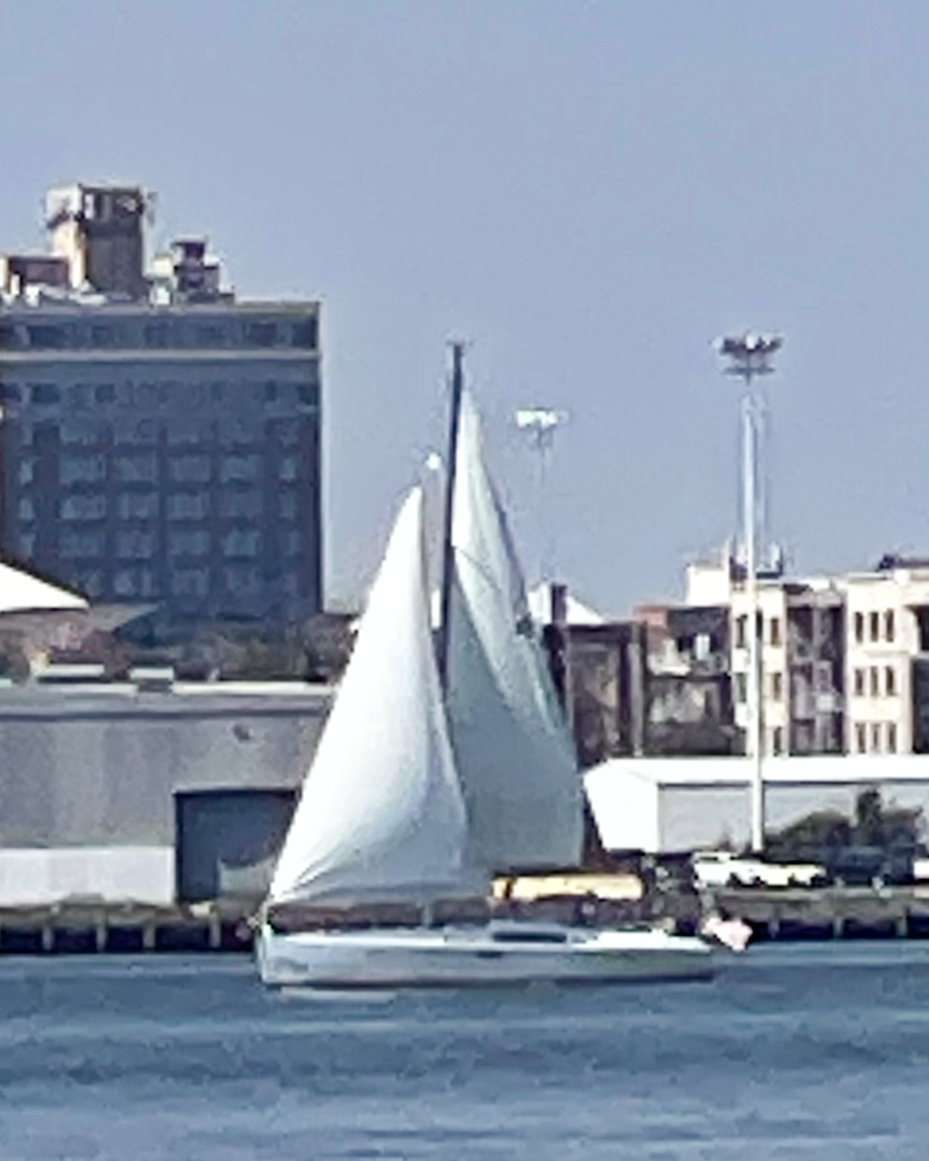 sailboat-gliding-on-calm-water-near-an-urban-shoreline-with-buildings-and-a-clear-sky