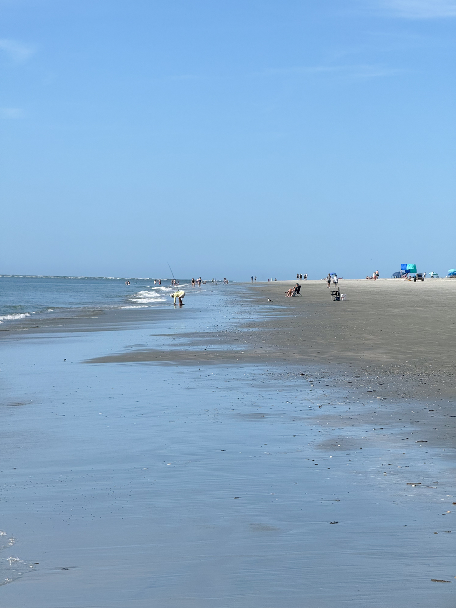 people-enjoying-a-sunny-day-on-a-wide-sandy-beach-with-gentle-waves-and-a-clear-blue-sky