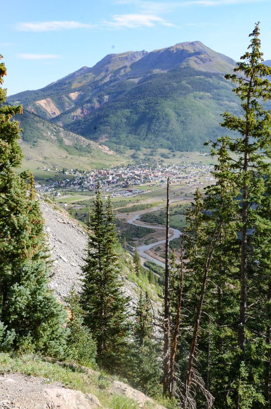 scenic-alpine-village-nestled-in-valley-below-rugged-snow-capped-peaks-and-pine-forests