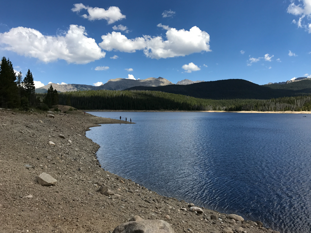 scenic-rocky-shoreline-of-alpine-lake-with-snow-capped-peaks-and-dramatic-cloudy-sky