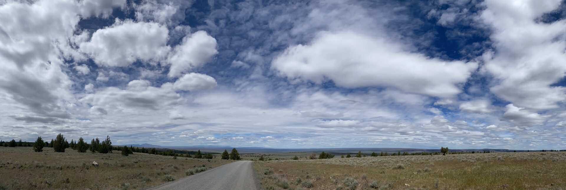 wide-open-landscape-expansive-blue-cloudy-sky-remote-rural-road-idyllic-scenic-route-view