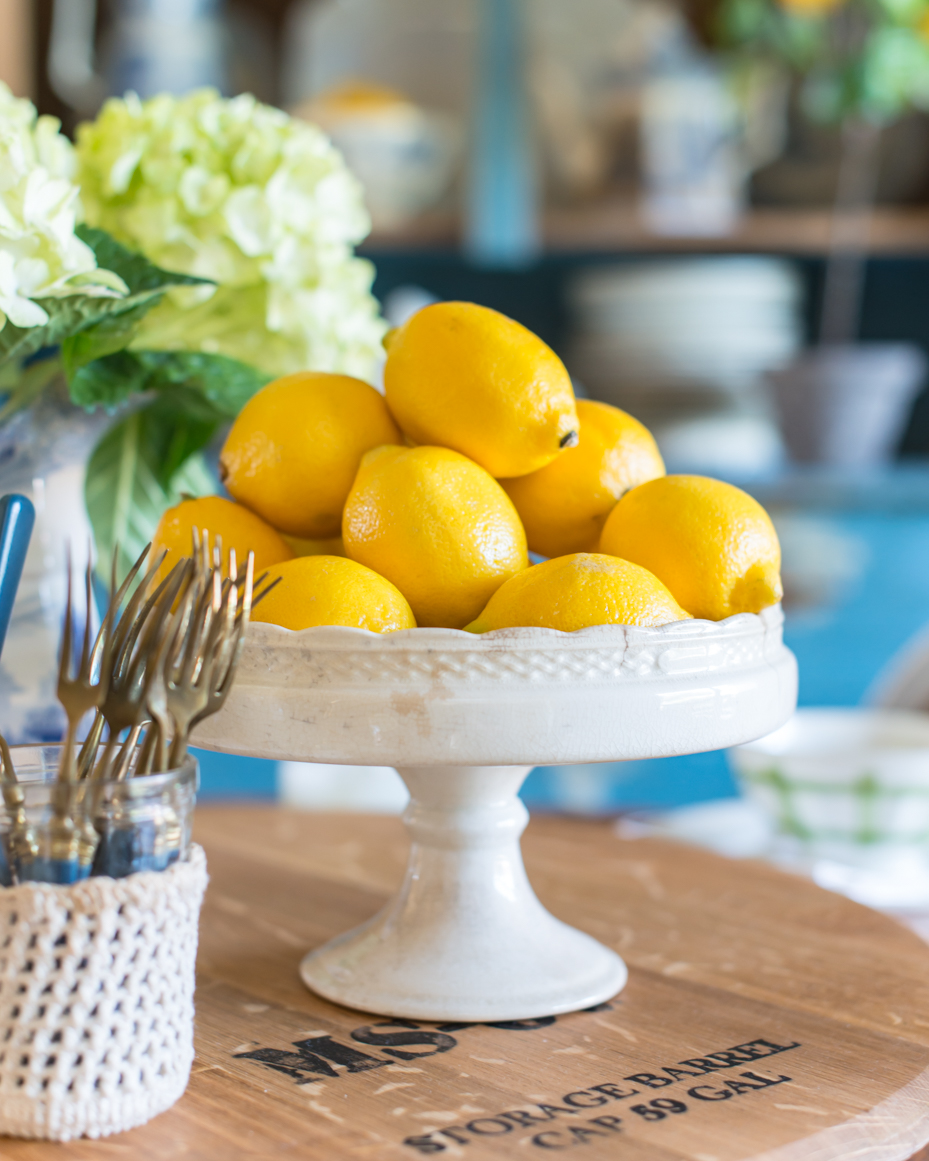 bright-yellow-lemons-on-white-pedestal-stand-with-rustic-kitchen-decor-royalty-free-reference-photo