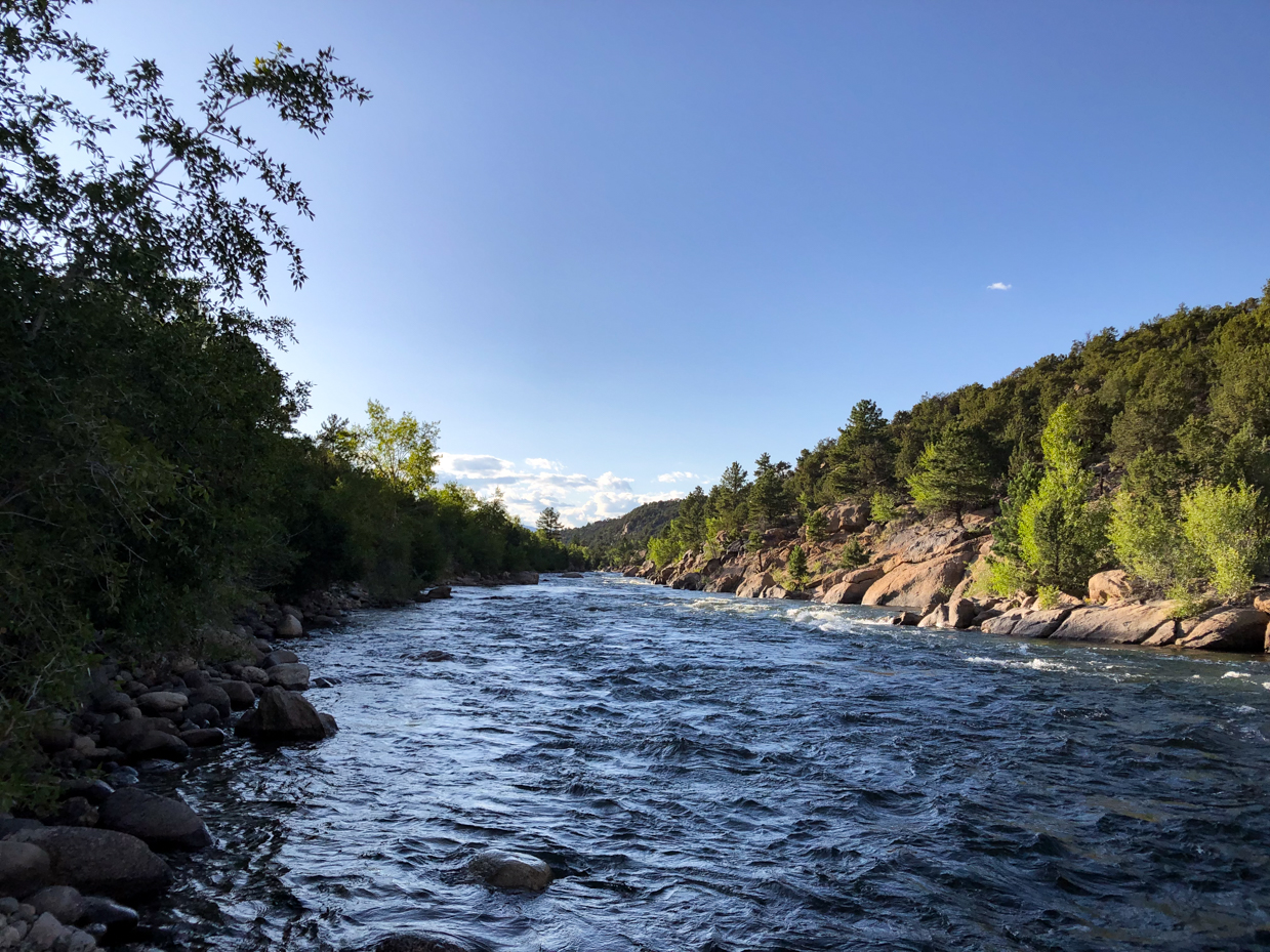 flowing-river-through-rocky-forested-landscape-under-clear-blue-skies