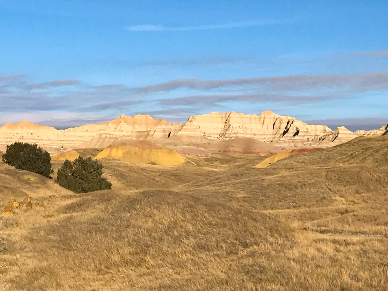 golden-prairie-and-striated-rock-formations-in-badlands-national-park-under-clear-blue-sky-royalty-free-landscape-reference-photo-for-desert-terrain-layered-geology-and-open-wilderness