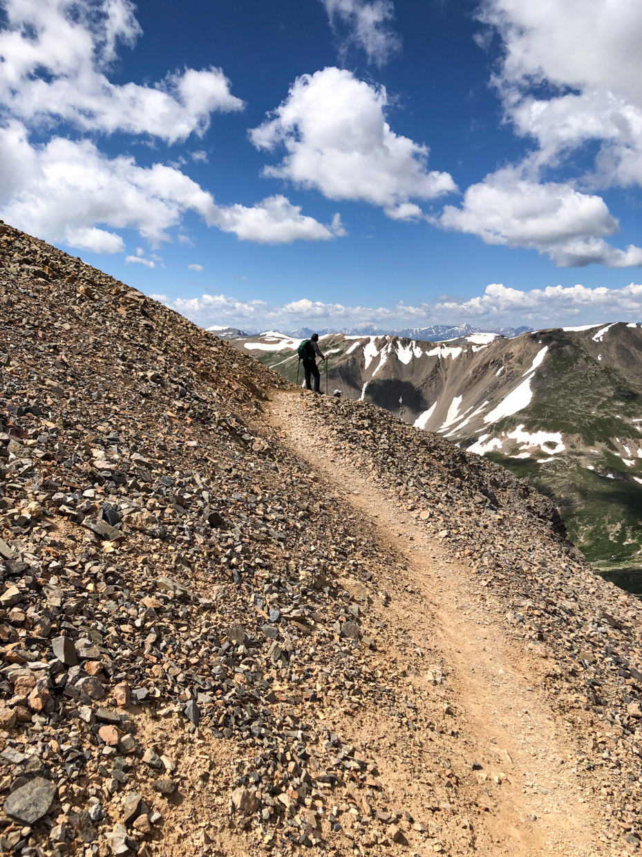 hiker-on-rocky-mountain-trail-with-stunning-snow-capped-peaks-and-blue-sky