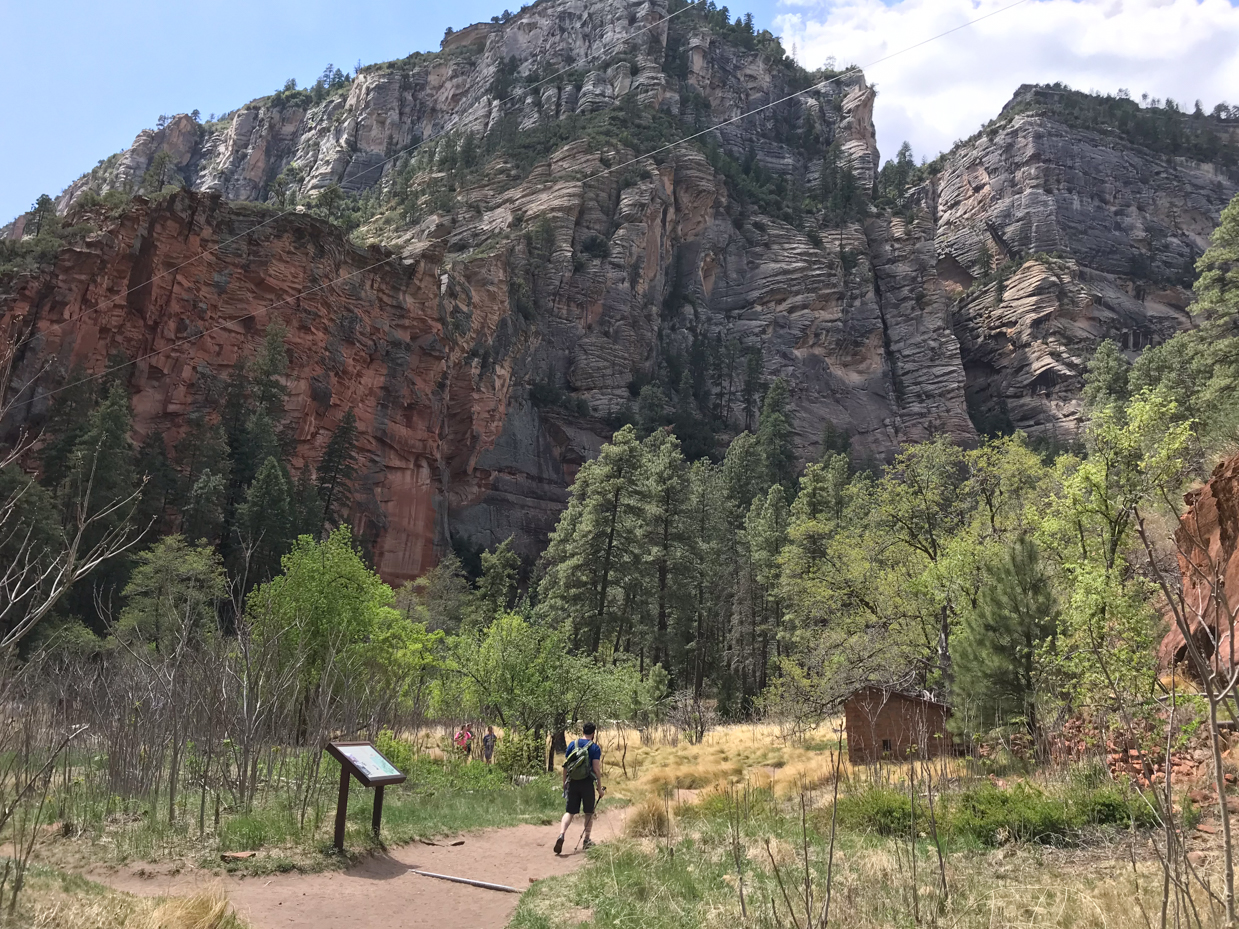 hiking-trail-through-red-rock-canyon-with-towering-cliffs-and-forested-landscape