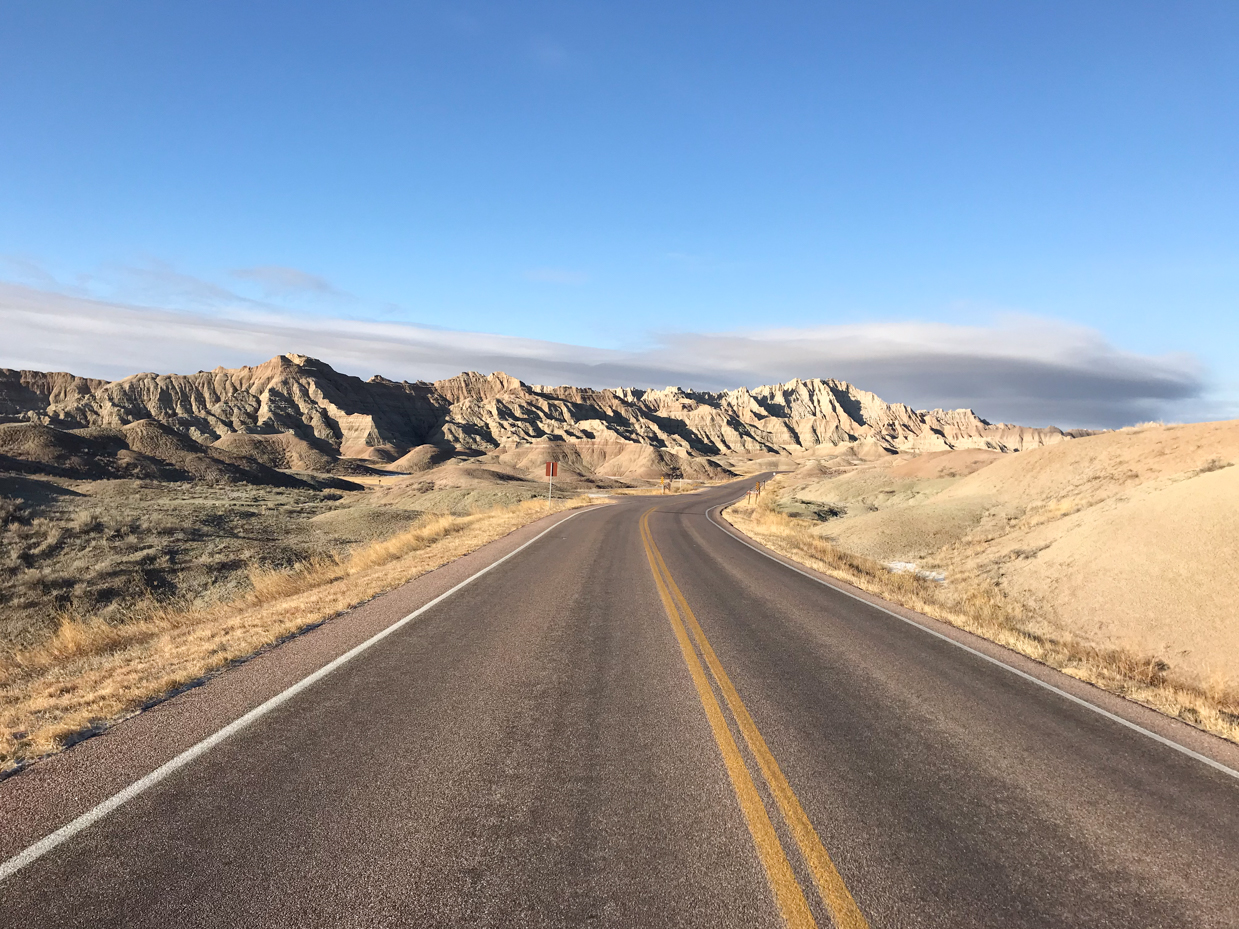 open-road-through-badlands-national-park-with-jagged-rock-formations-and-clear-blue-sky-royalty-free-travel-and-landscape-reference-photo-for-scenic-drives-rugged-terrain-and-desert-wilderness