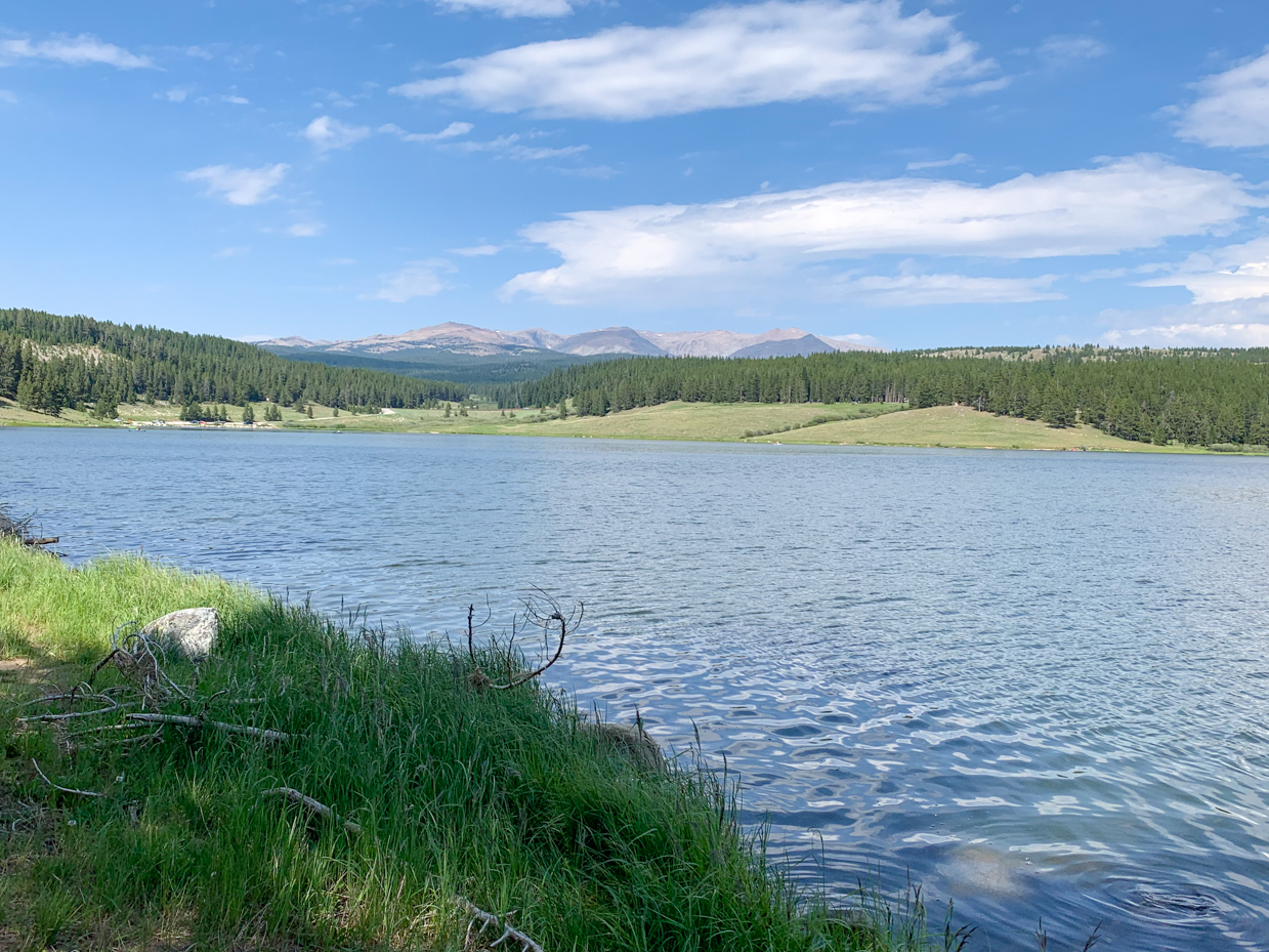 serene-lake-with-lush-green-shores-and-mountain-backdrop-under-clear-blue-sky-tranquil-nature-scene