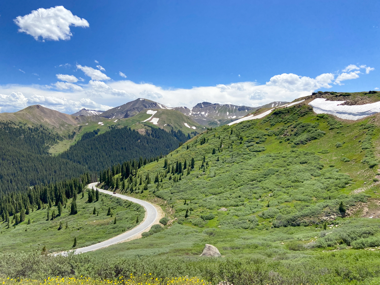 winding-mountain-road-through-green-alpine-meadows-with-snow-capped-peaks-under-clear-blue-sky-royalty-free-landscape-reference-photo-for-scenic-drives-wilderness-and-outdoor-adventure