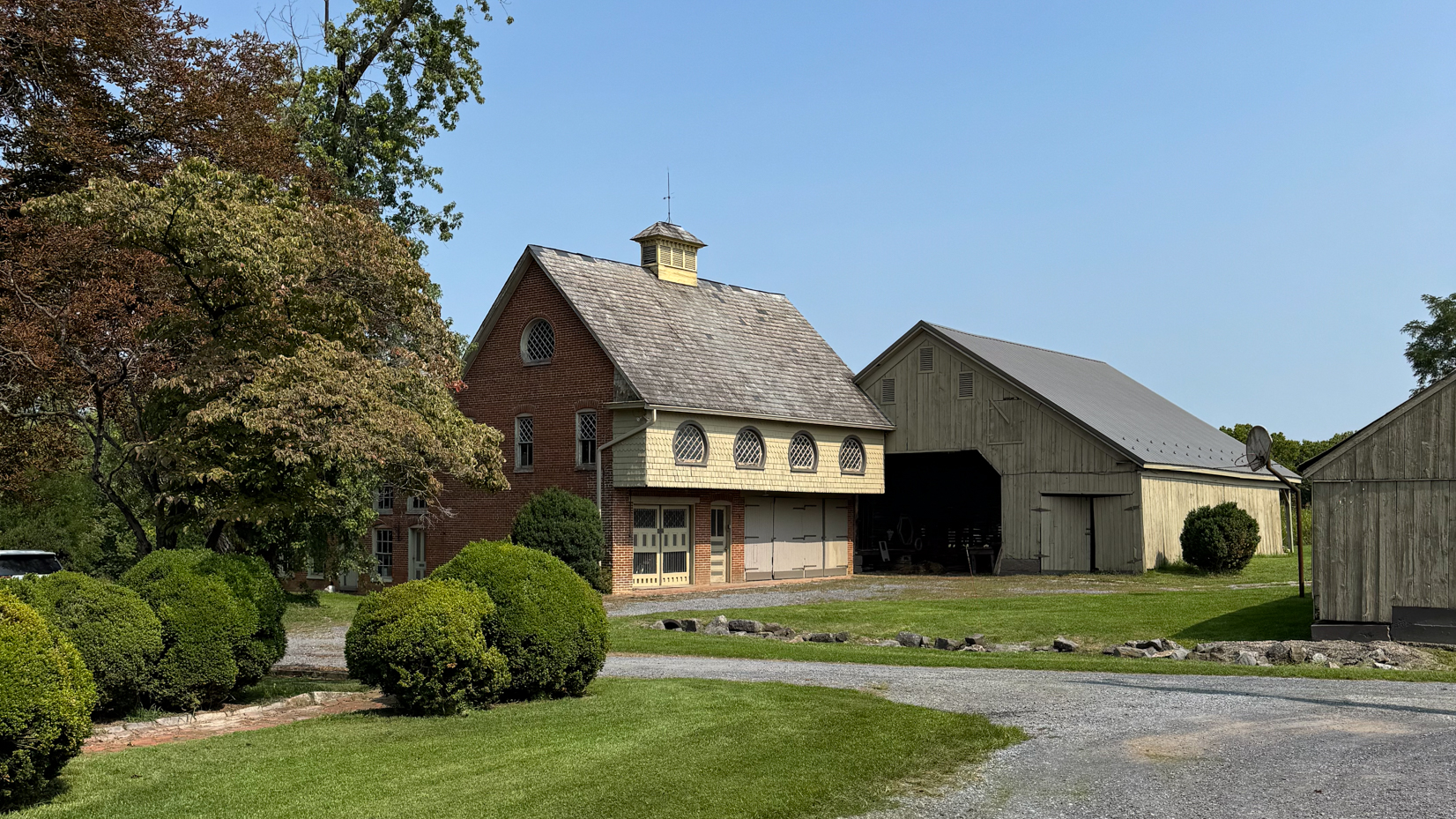 brick-and-wood-barns-on-a-farm-surrounded-by-neatly-trimmed-bushes-and-trees