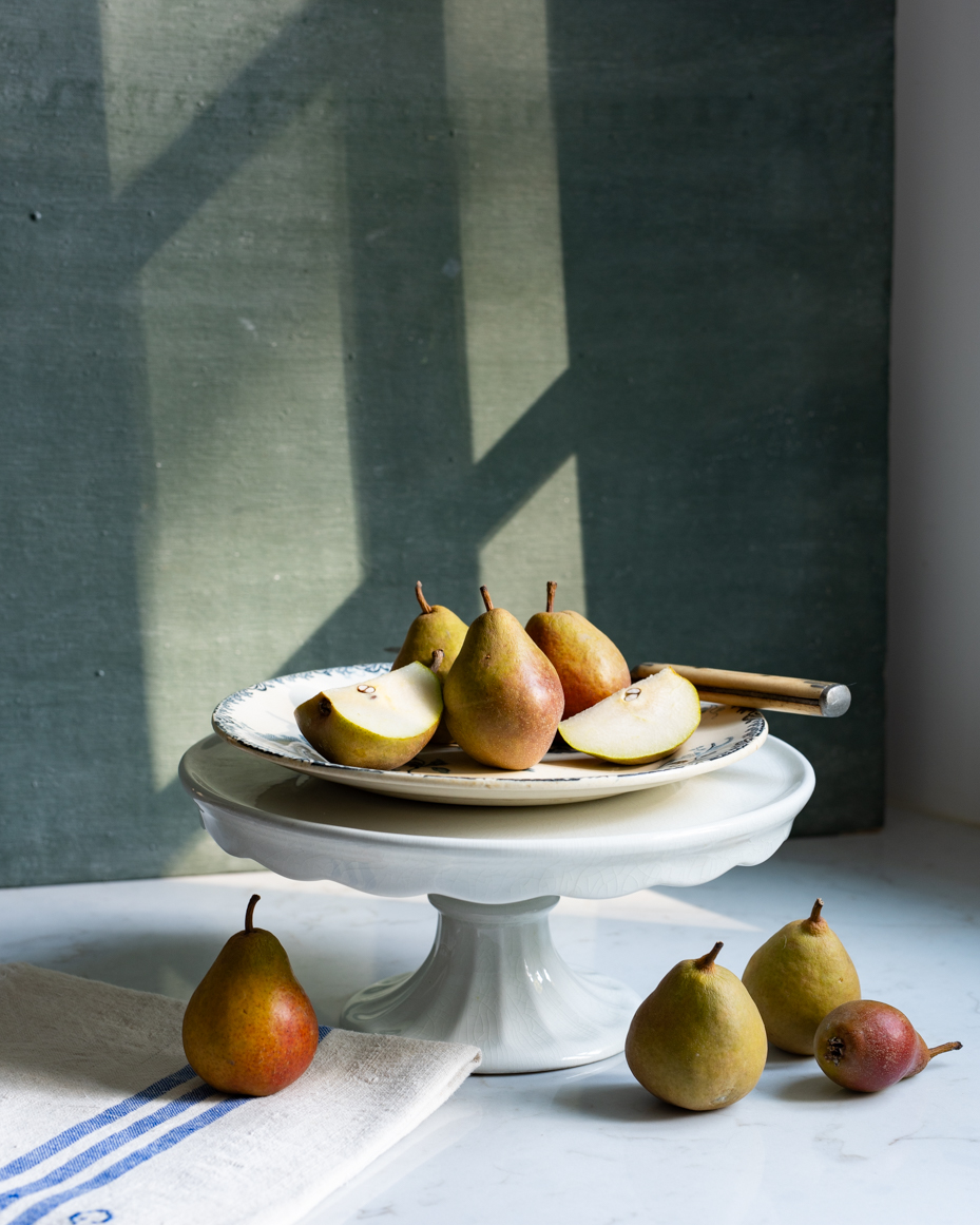 elegant-pear-still-life-on-cake-stand-with-linen-and-sunlit-background