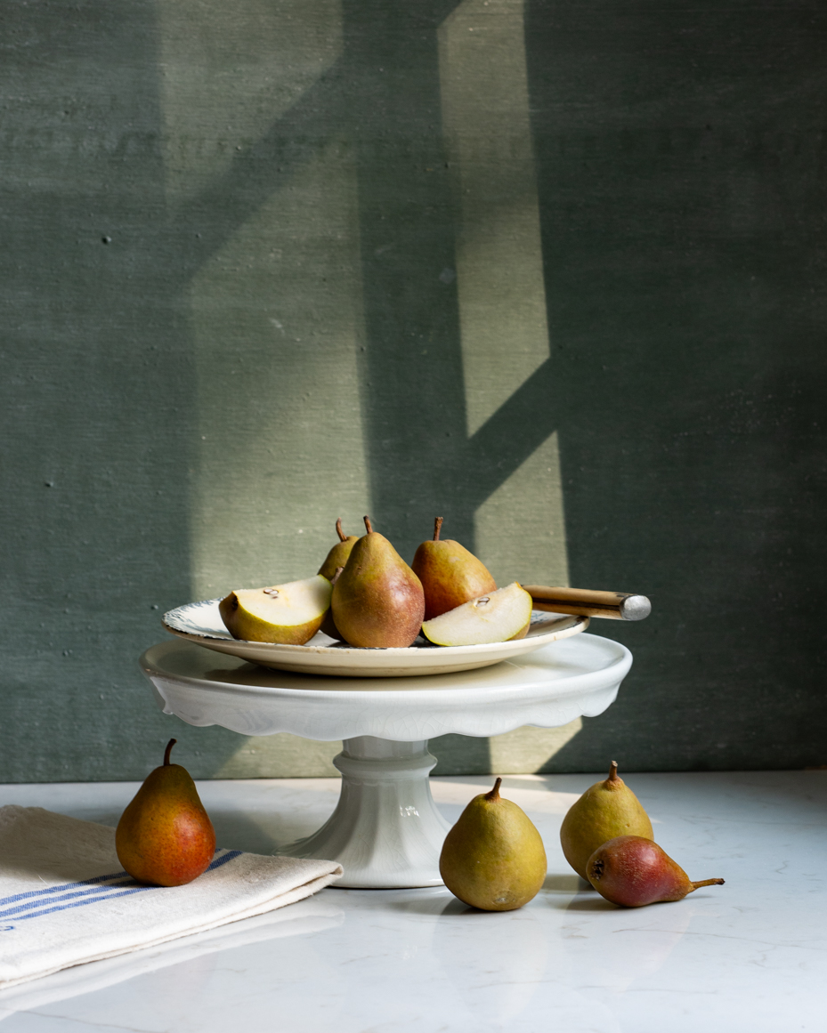 rustic-pear-still-life-on-cake-stand-with-sunlit-shadows-and-linen