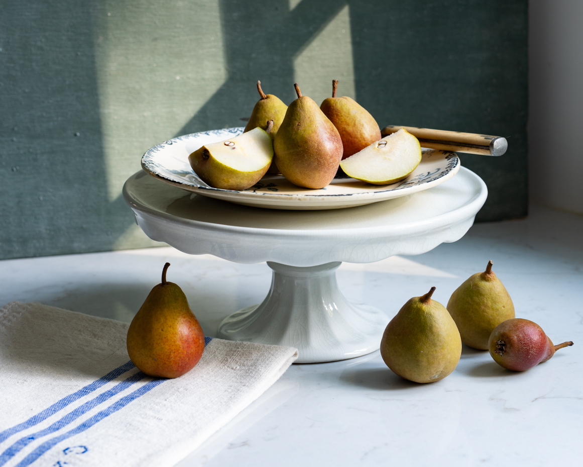 rustic-pears-on-plate-with-cake-stand-and-linen-natural-light-still-life