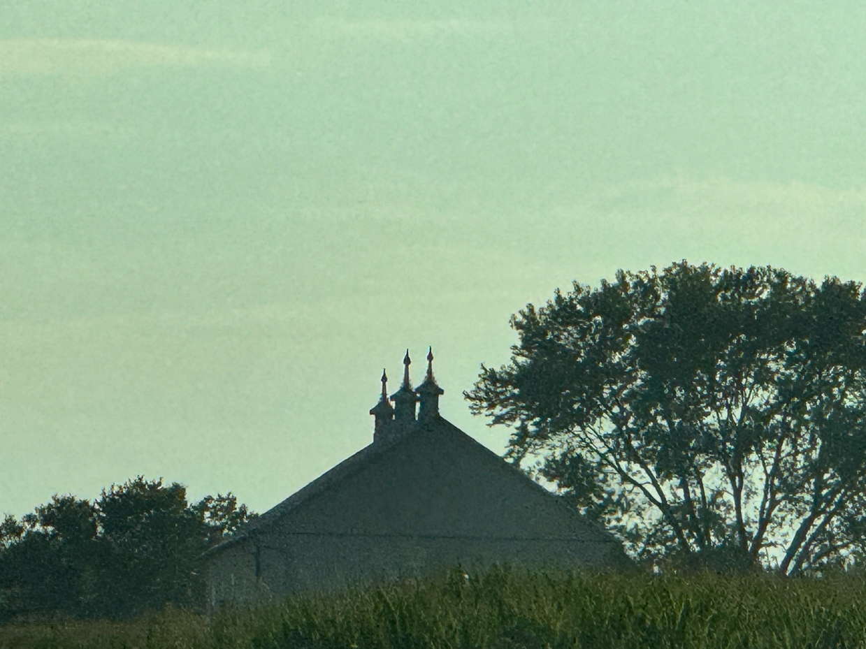 silhouette-of-a-barn-with-three-prominent-cupolas-and-lush-trees-against-a-soft-sky-in-the-evening-light