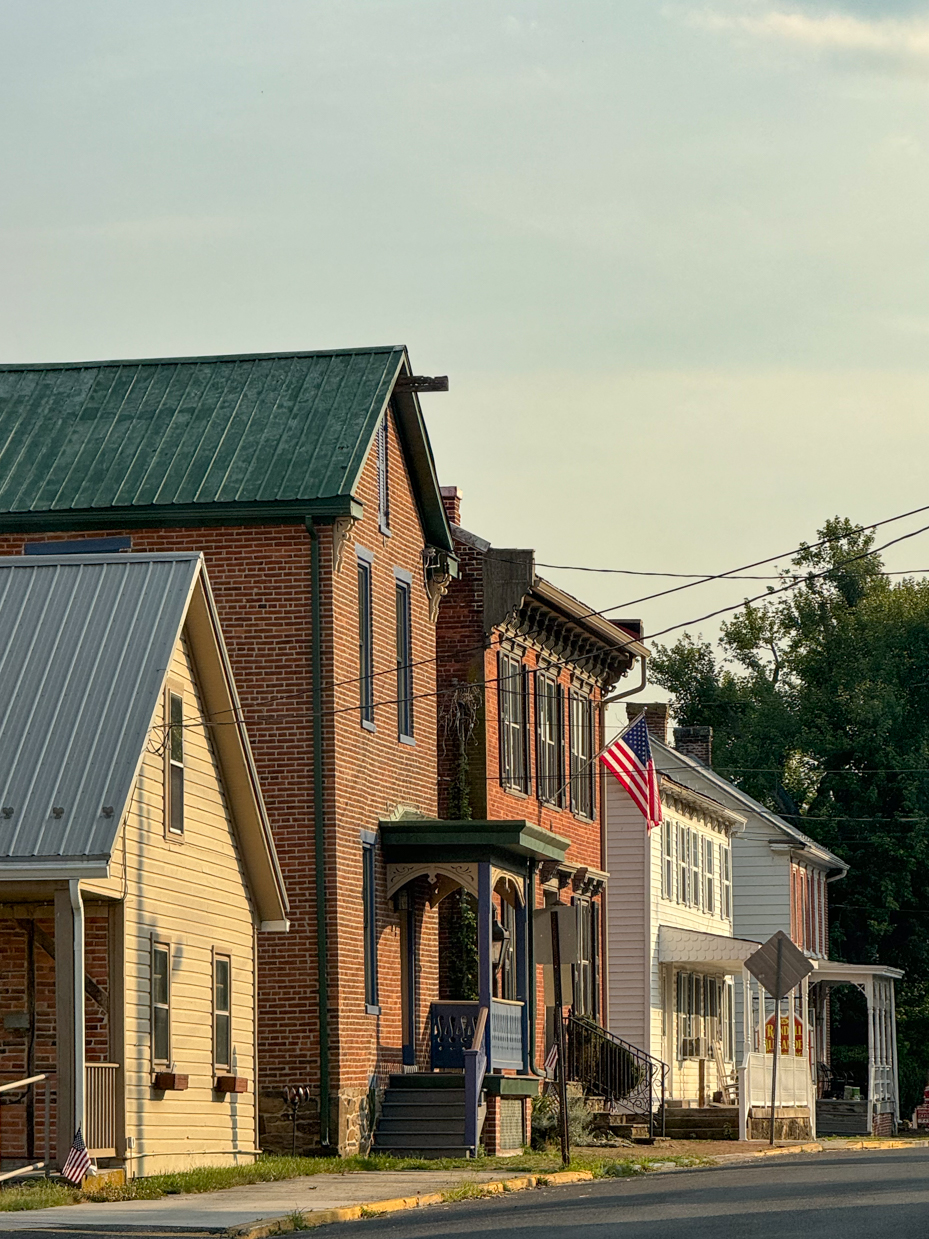 the-sunlight-gently-illuminates-the-classic-facades-of-a-row-of-historic-homes-in-a-quiet-american-town-featuring-cozy-porches-and-proudly-displayed-flags