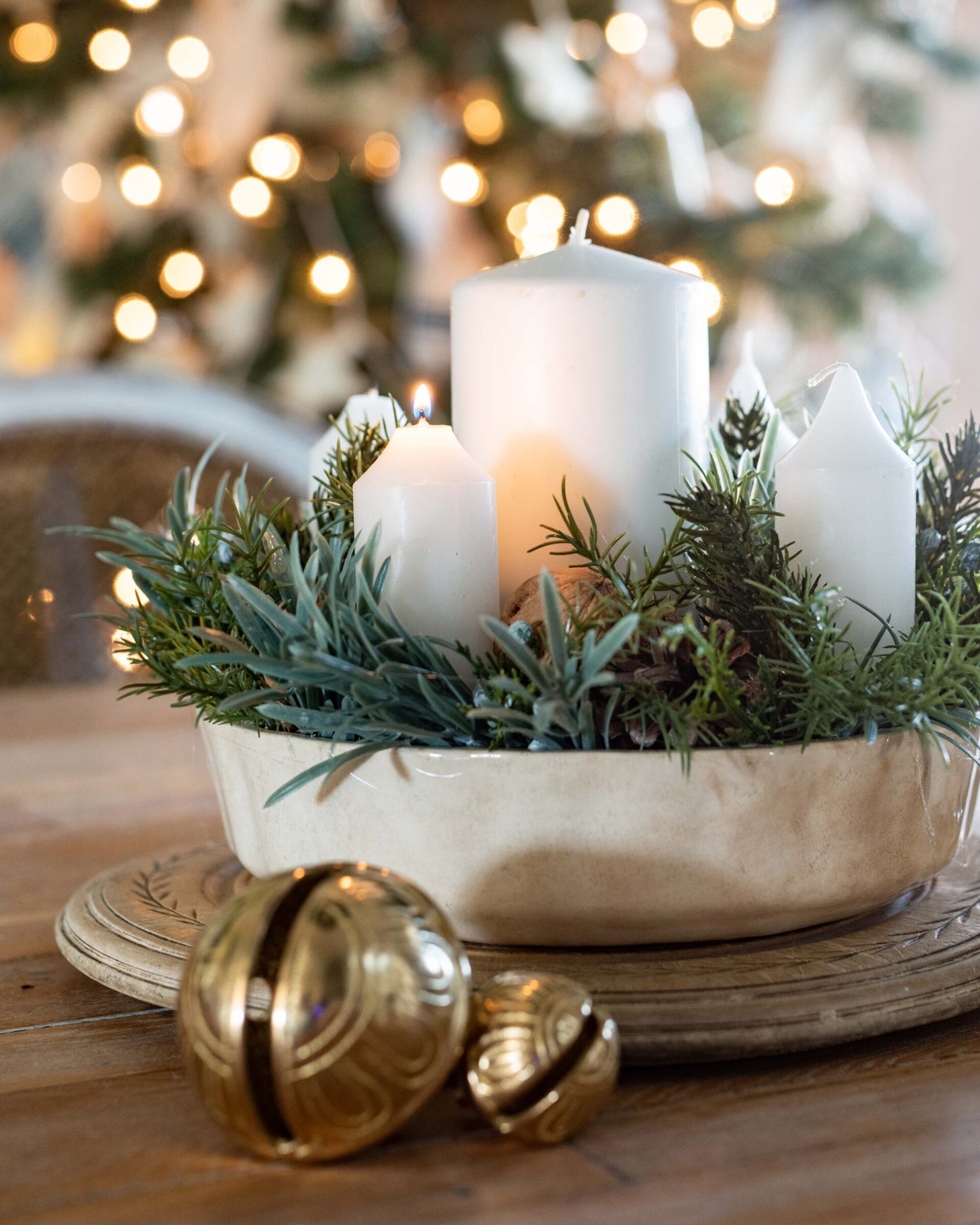 an-elegant-holiday-centerpiece-featuring-white-pillar-candles-nestled-in-a-vintage-ceramic-dish-filled-with-fresh-evergreen-sprigs-set-atop-an-antique-gold-pedestal-with-blurred-christmas-tree-lights