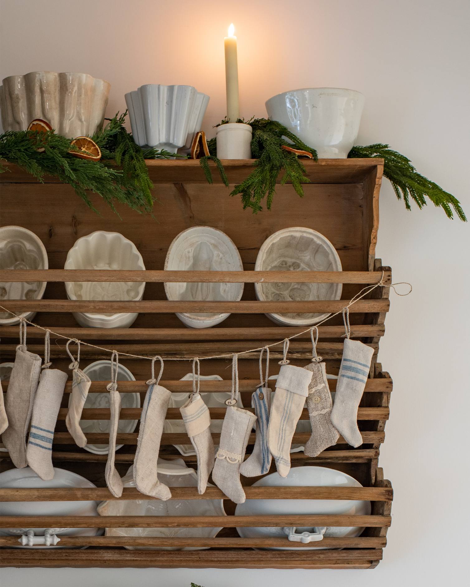 antique-wooden-rack-with-mini-linen-christmas-stockings-vintage-white-ceramics-fresh-greenery-dried-orange-slices-and-candle