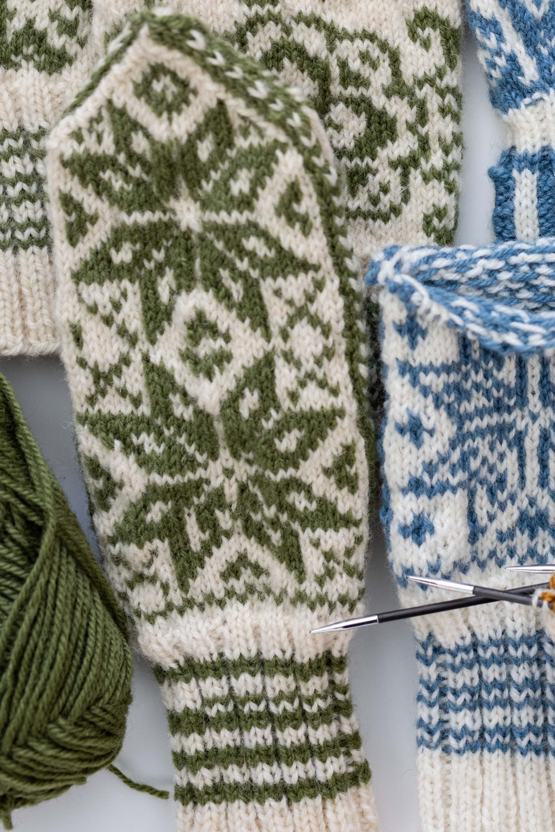 close-up-of-hand-knitted-mittens-with-green-nordic-snowflake-pattern-and-knitting-needles