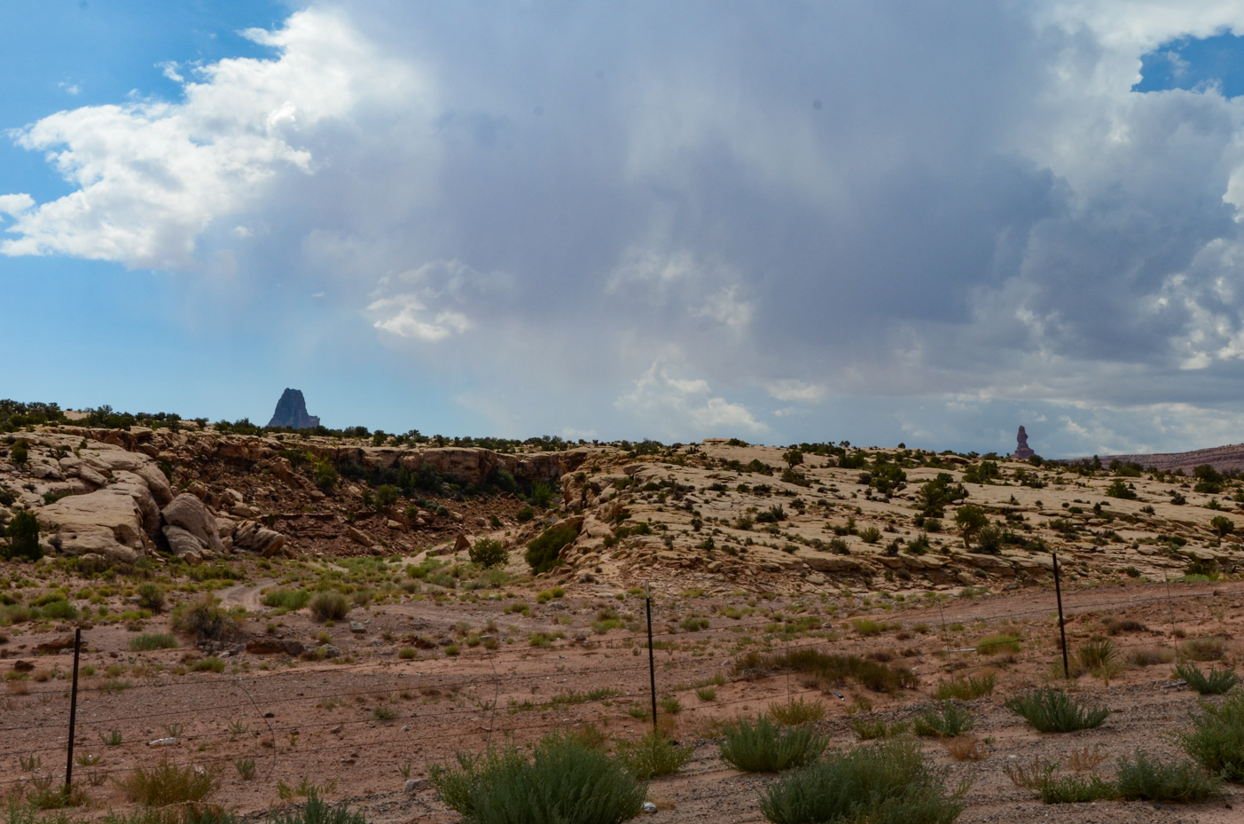 distant-monoliths-rising-above-rugged-desert-terrain-under-dramatic-storm-clouds