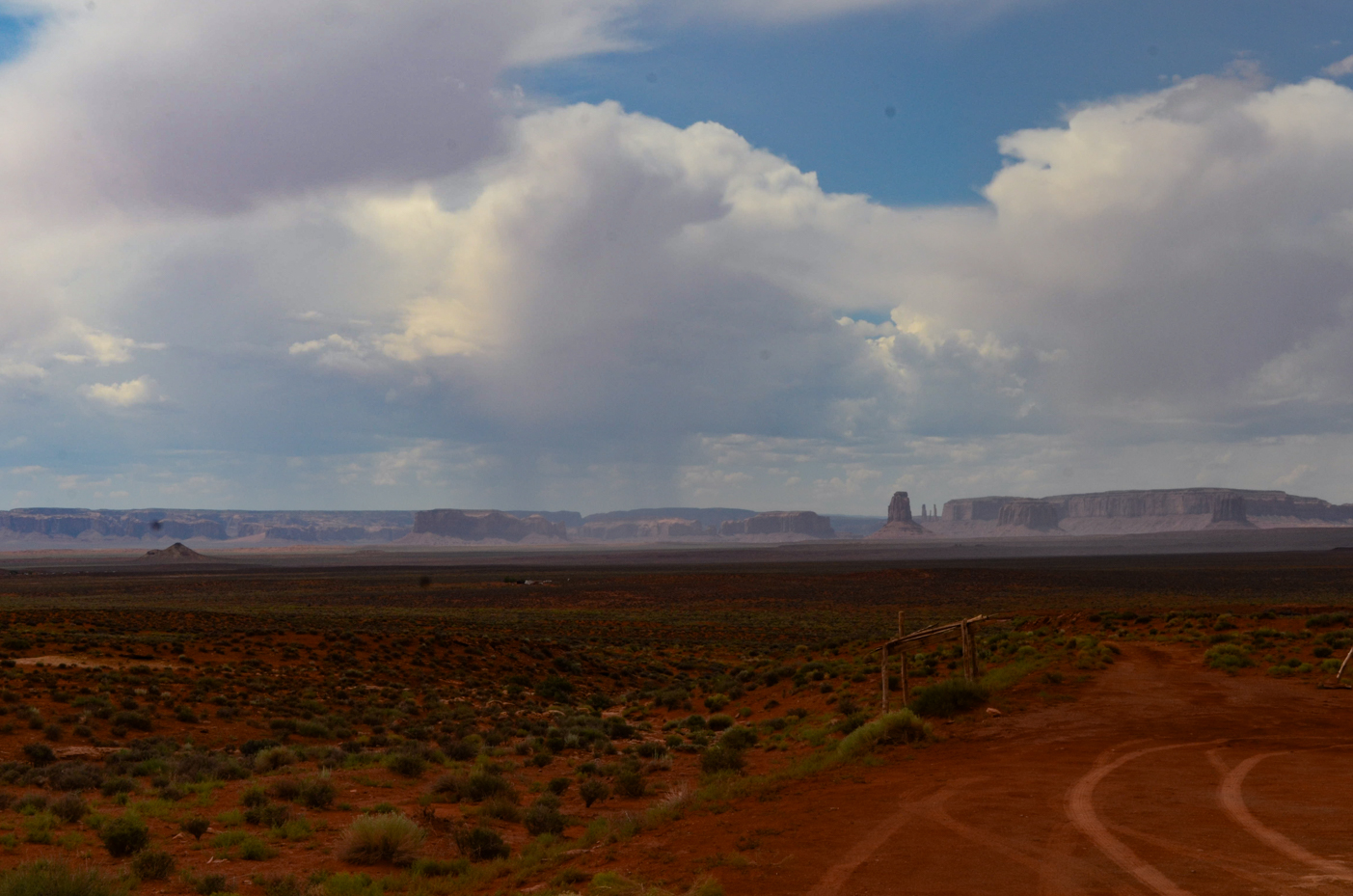 distant-monument-valley-buttes-beneath-towering-storm-clouds-over-vast-desert-plateau