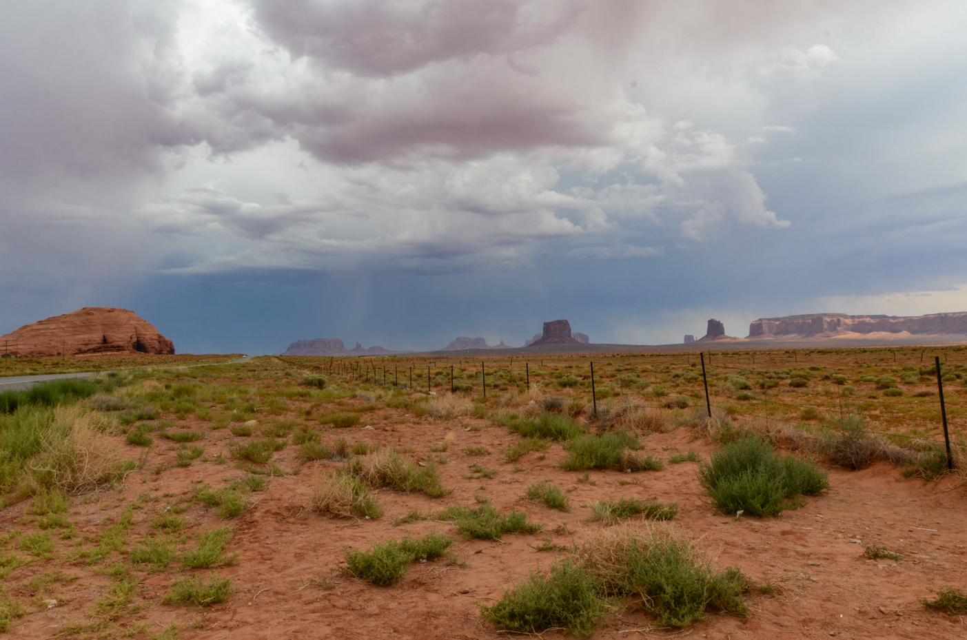 distant-monument-valley-mesas-under-dramatic-storm-clouds-with-sparse-desert-vegetation