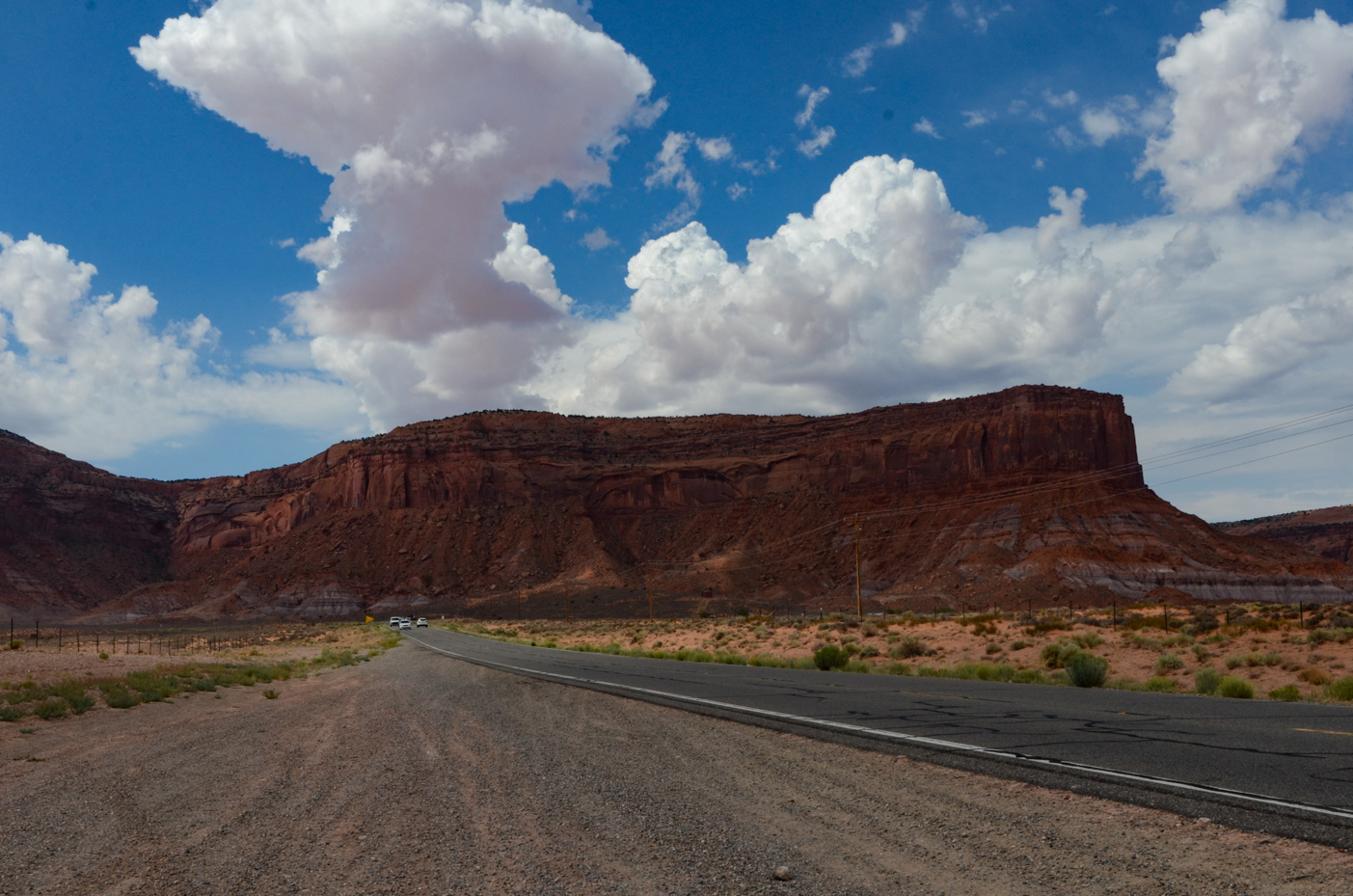 expansive-monument-valley-butte-towering-over-winding-desert-highway-under-fluffy-clouds