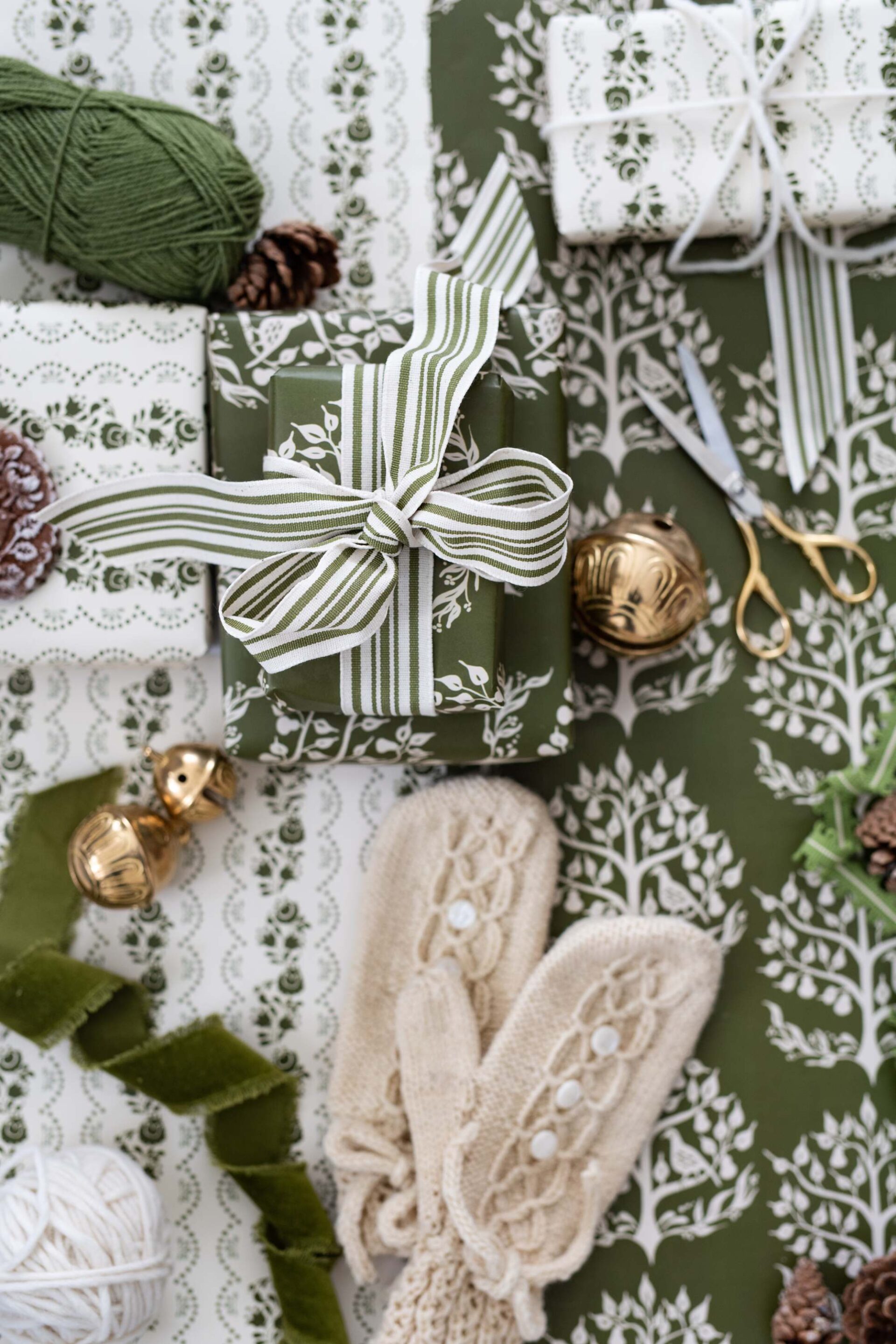 festive-gift-boxes-wrapped-in-lace-patterned-paper-with-greenery-and-bells