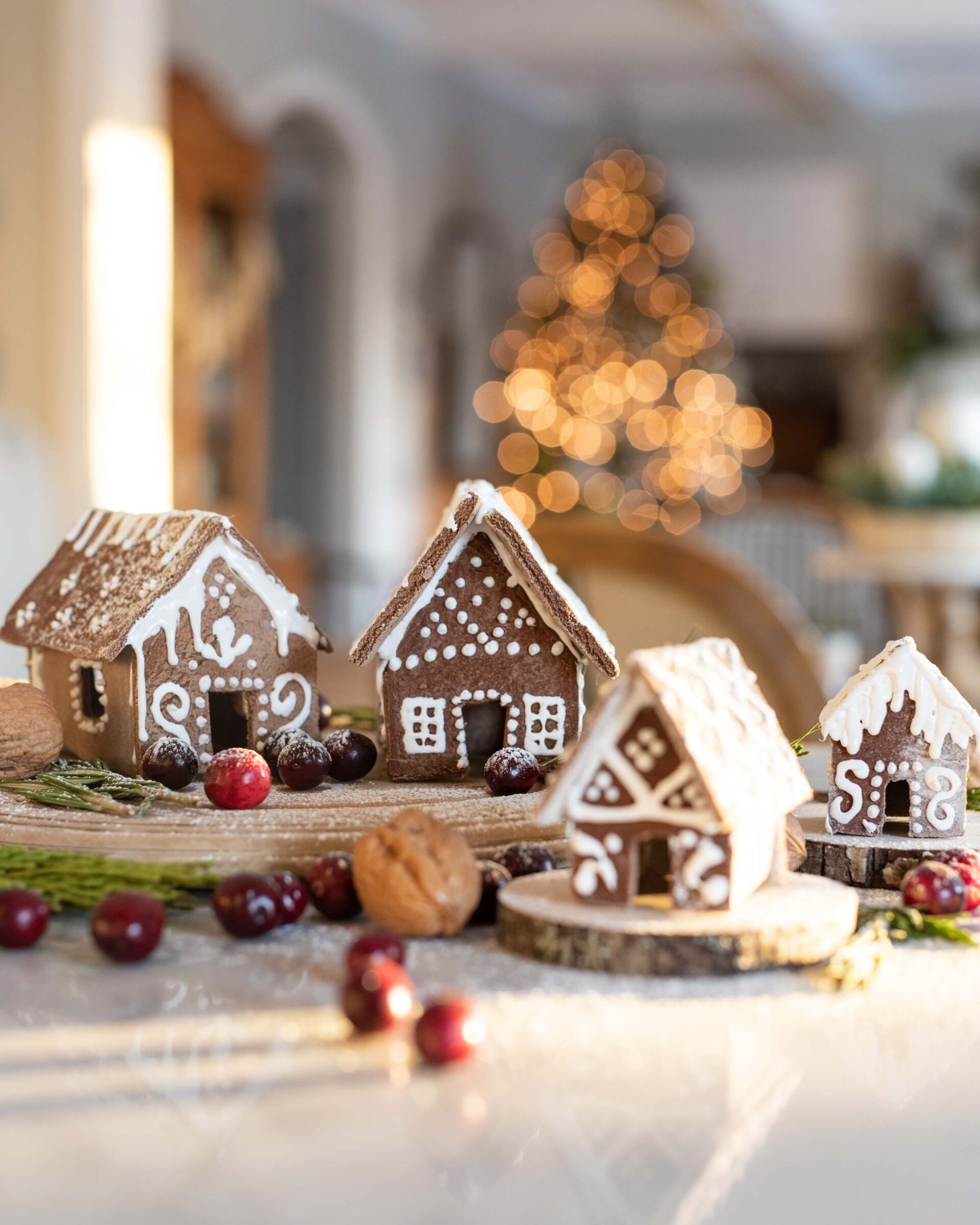 festive-gingerbread-house-village-with-icing-sprinkles-and-walnuts-on-rustic-wooden-pedestal-with-blurred-christmas-tree-lights-in-background