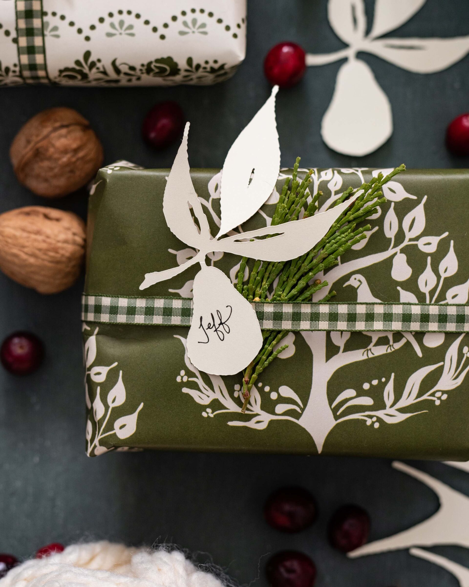 festive-holiday-gift-wrapping-with-papercut-foliage-design-personalized-tags-and-rustic-embellishments-on-dark-background-with-scattered-cranberries-and-walnuts