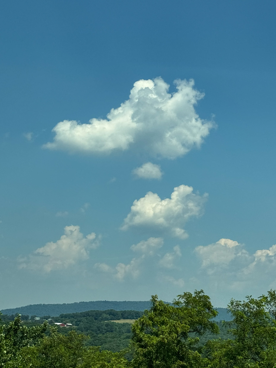 fluffy-white-clouds-on-a-clear-blue-sky-over-green-hills-serene-nature-scene-royalty-free-reference-photo