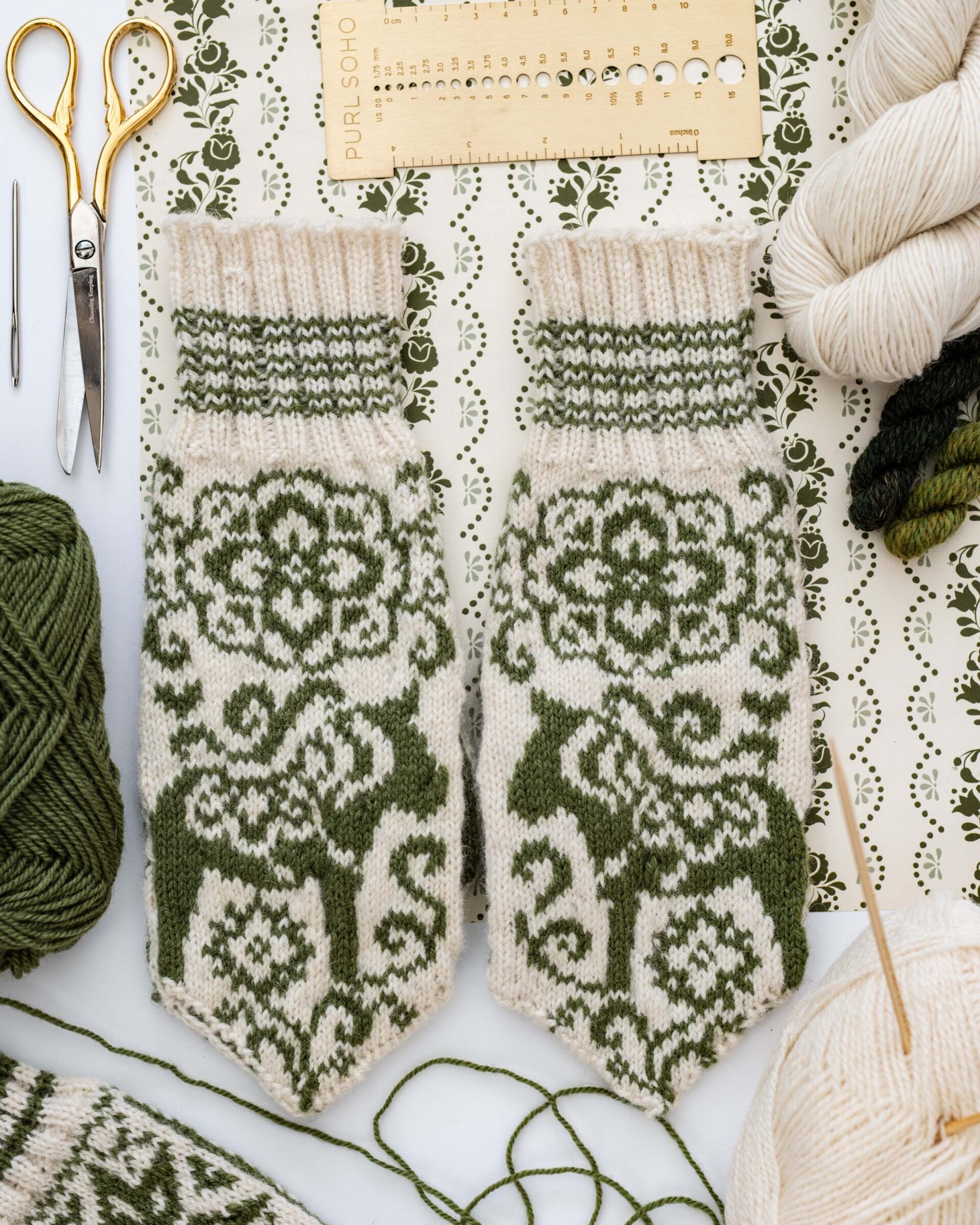 hand-knitted-mittens-with-green-nordic-deer-pattern-and-crafting-tools-flat-lay