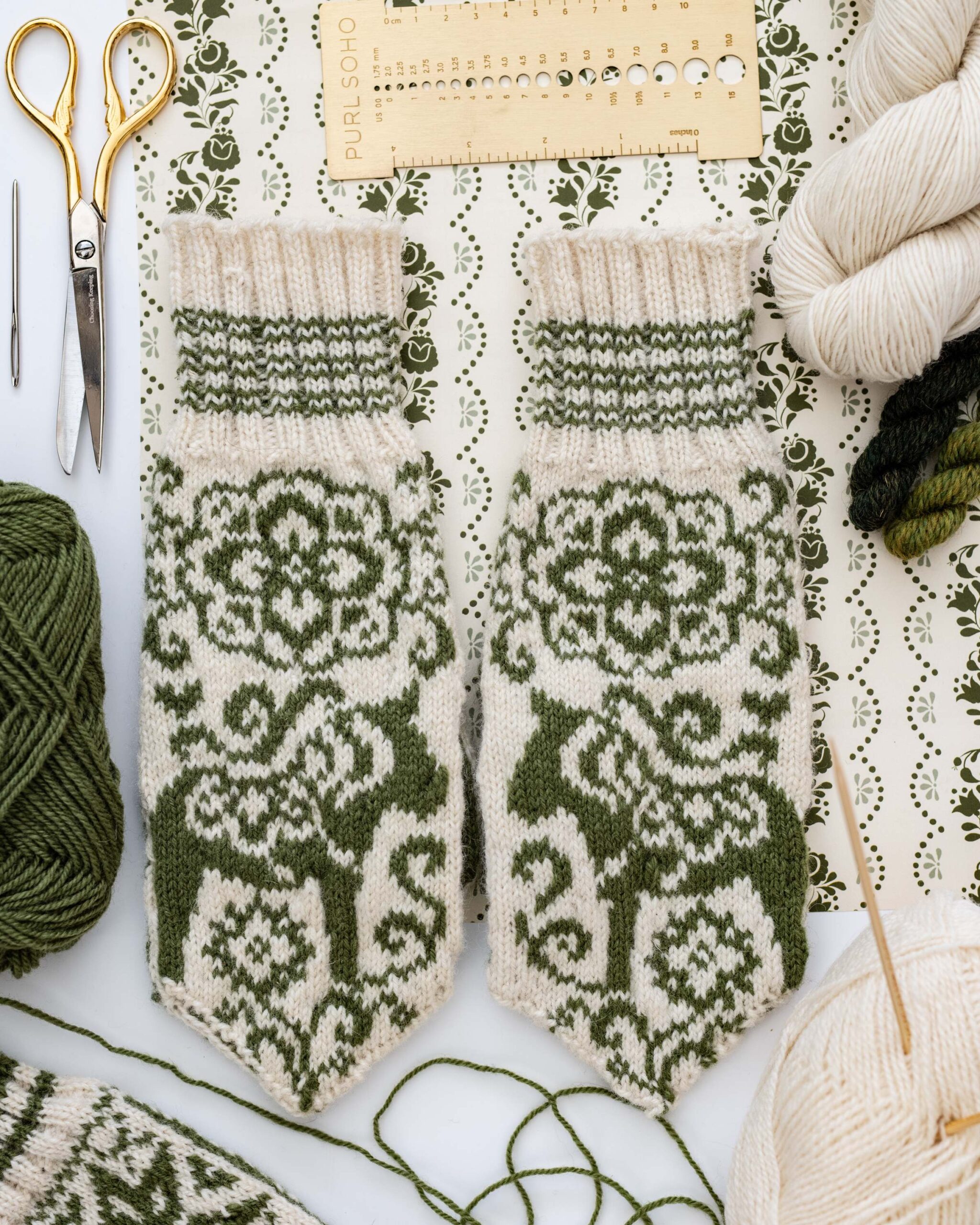 Hand-Knitted Mittens with Green Nordic Deer Pattern and Crafting Tools Flat Lay artist reference photo