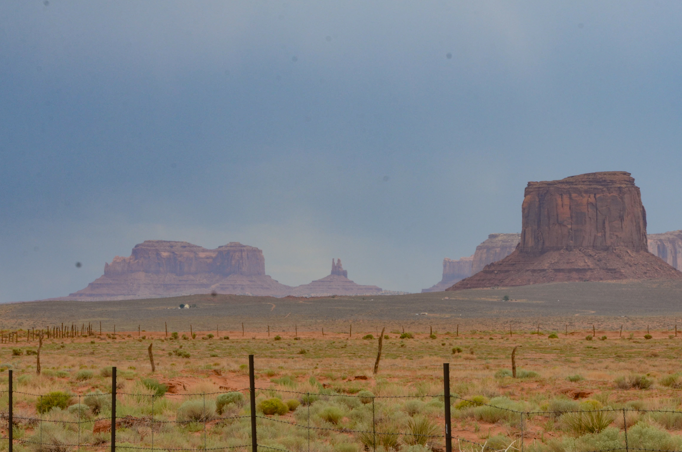 iconic-monument-valley-buttes-rising-above-fenced-desert-plain-under-hazy-blue-sky