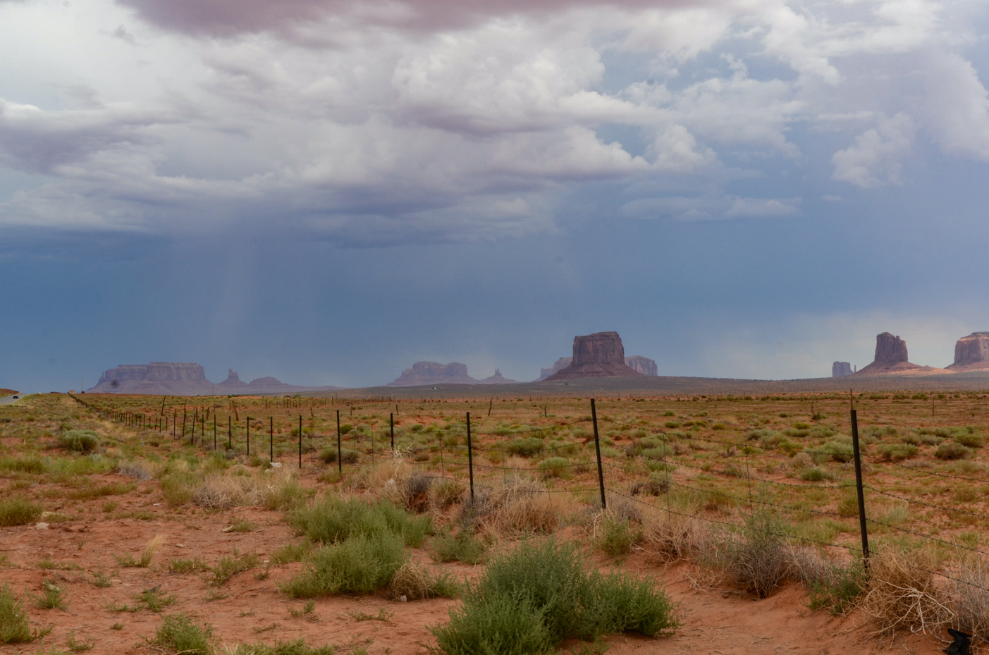 iconic-monument-valley-buttes-rising-above-fenced-desert-plains-under-dramatic-stormy-sky