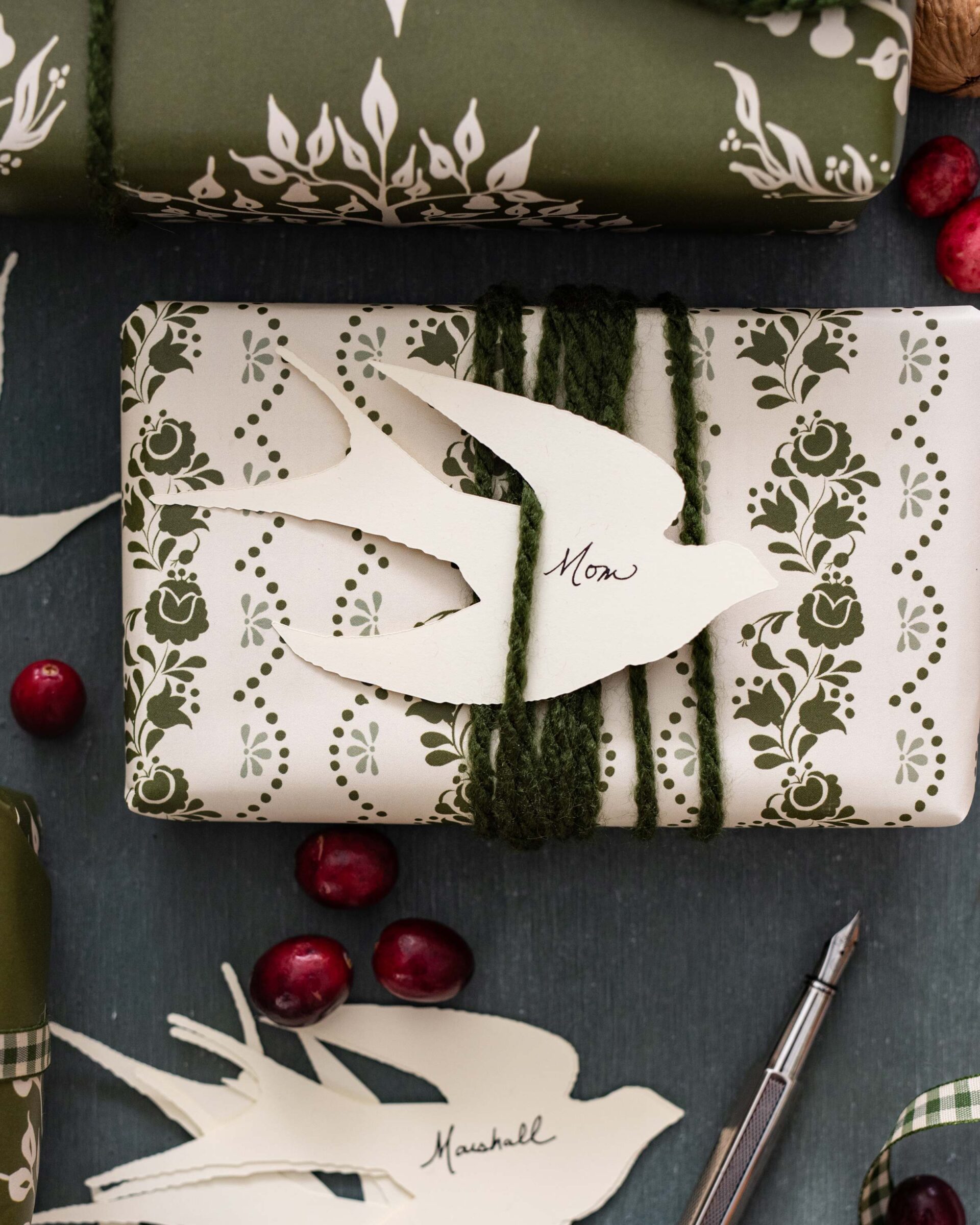 olive-green-holiday-gift-wrap-with-vintage-floral-pattern-personalized-dove-tags-and-trailing-greenery-accents-on-dark-rustic-background-with-fresh-cranberries