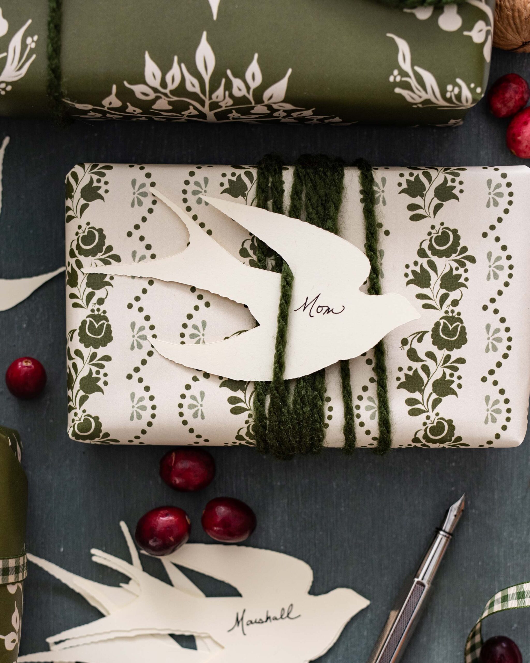 Olive Green Holiday Gift Wrap with Vintage Floral Pattern, Personalized Dove Tags and Trailing Greenery Accents on Dark Rustic Background with Fresh Cranberries artist reference photo