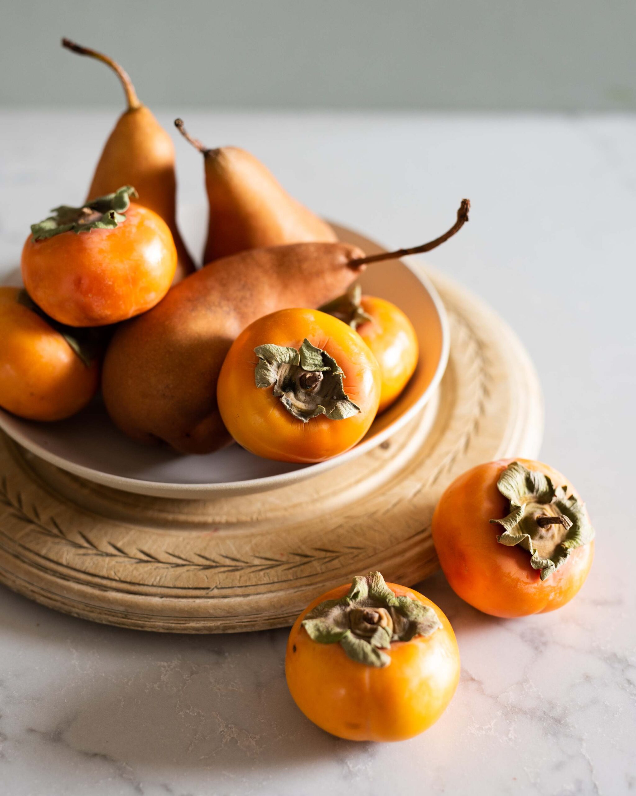 Persimmons on a white plate, some sliced open to reveal textured interior and topped with leafy garnish artist reference photo