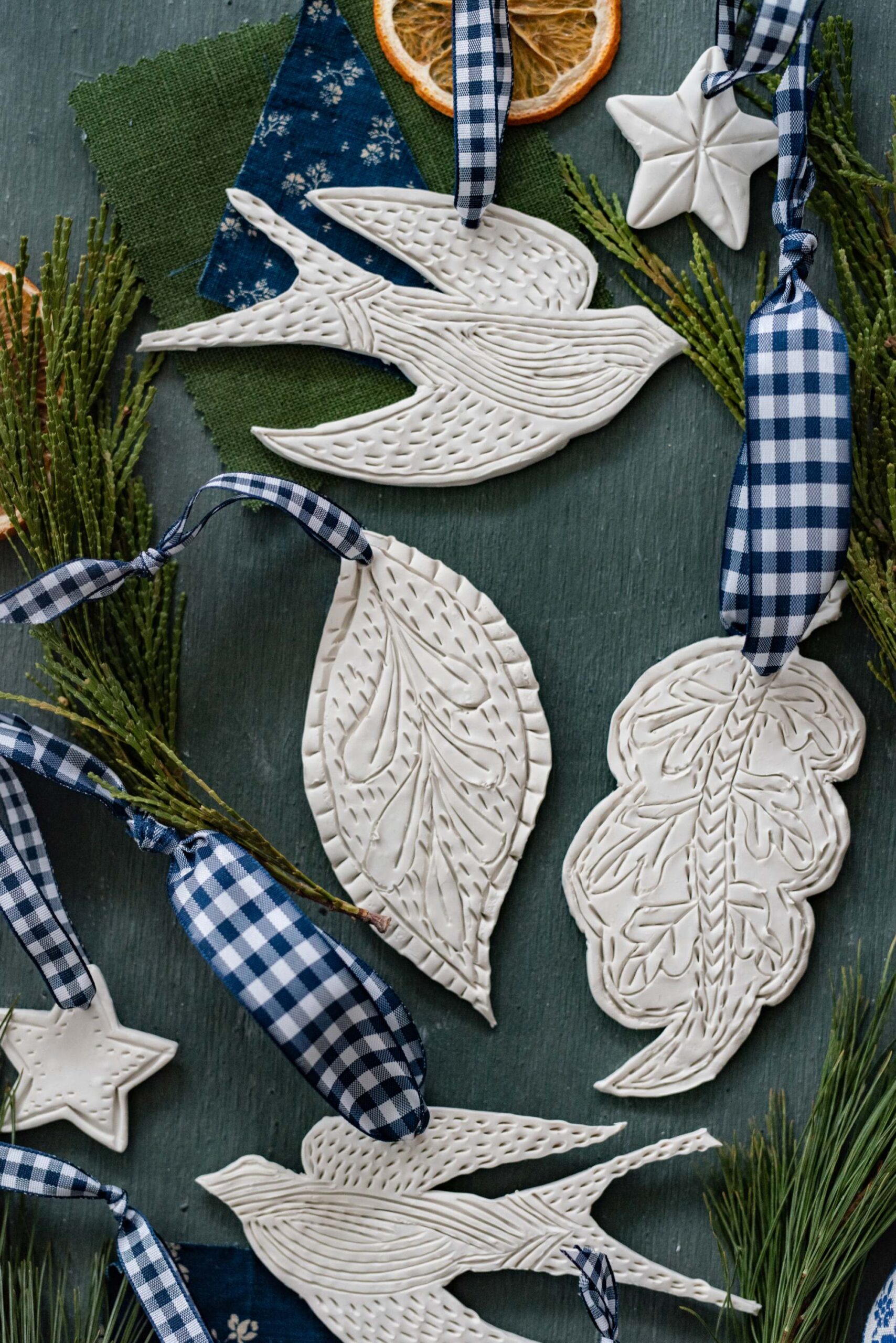 Rustic Christmas Ornaments – Ceramic White Doves and Textured Leaves with Blue Gingham Ribbon on Evergreen Background artist reference photo