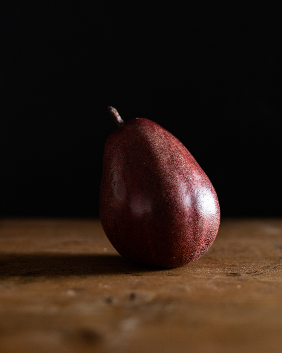 single-red-pear-on-wooden-surface-with-dark-background-elegant-minimalist-photography