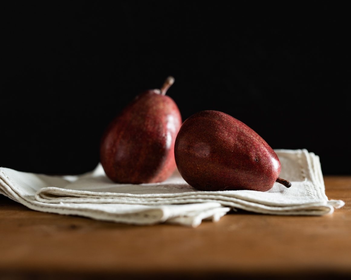 two-red-pears-on-folded-linen-napkins-rustic-still-life-photography-with-dark-background