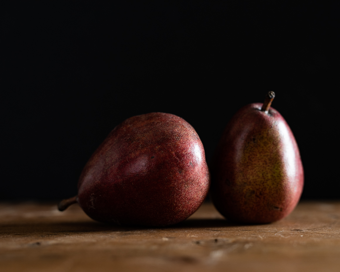 two-red-pears-on-wooden-surface-with-dark-background-minimalist-food-photography