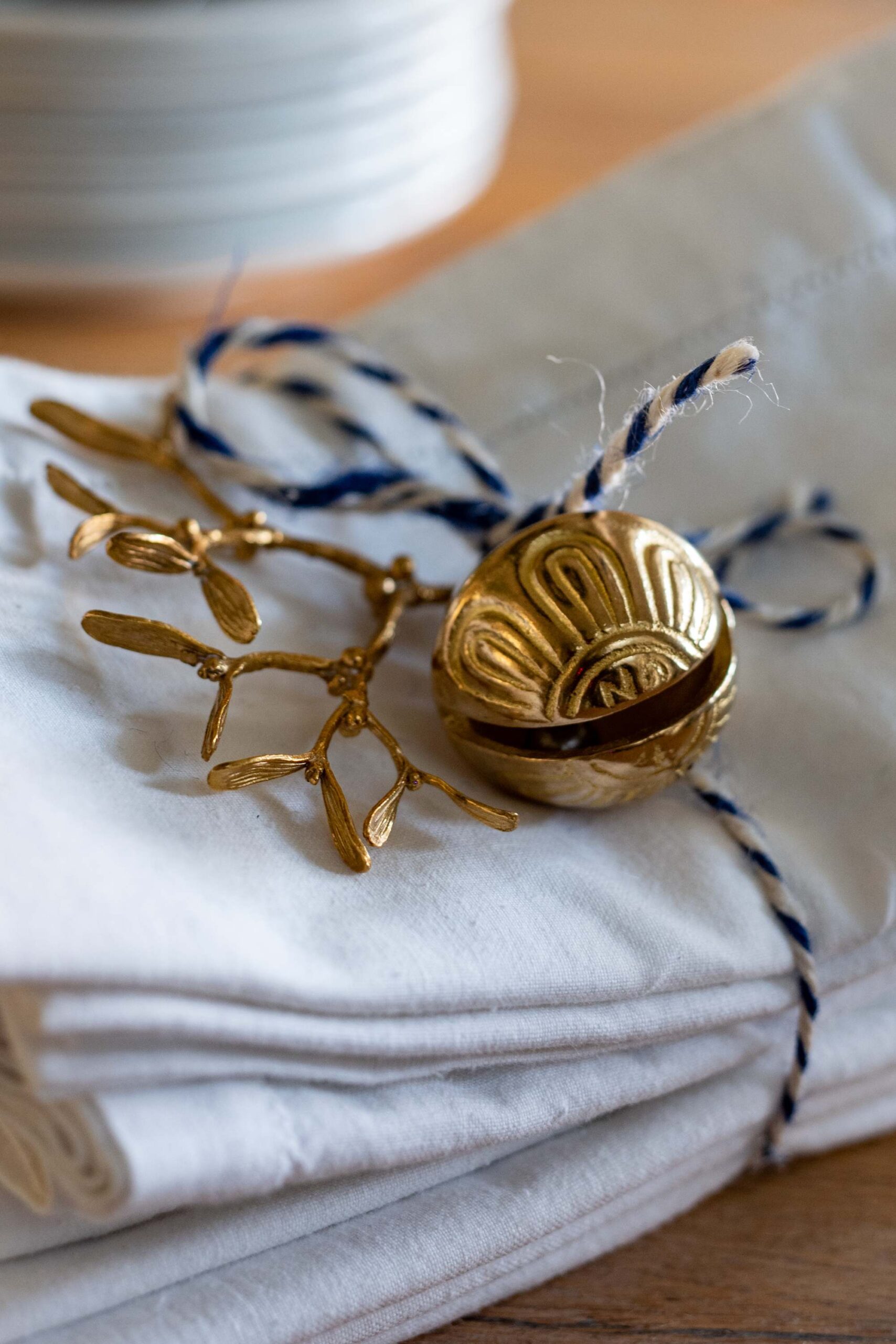 Two vintage brass Christmas ornaments, one shaped like a tree branch and the other like a scallop shell, tied with navy blue and white baker’s twine and placed on folded white linen napkins artist reference photo
